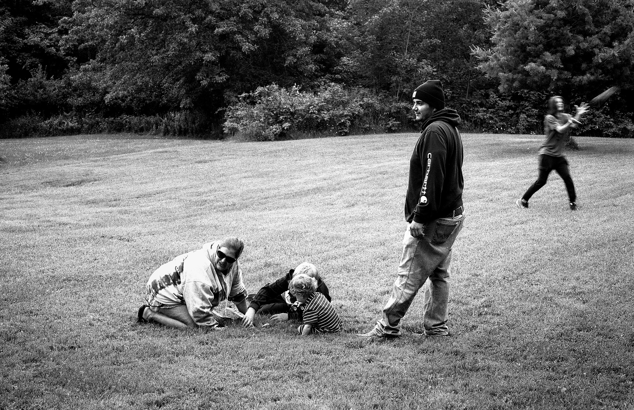 Family playing in large grassy field adults and children on lawn with dense forest treeline in background