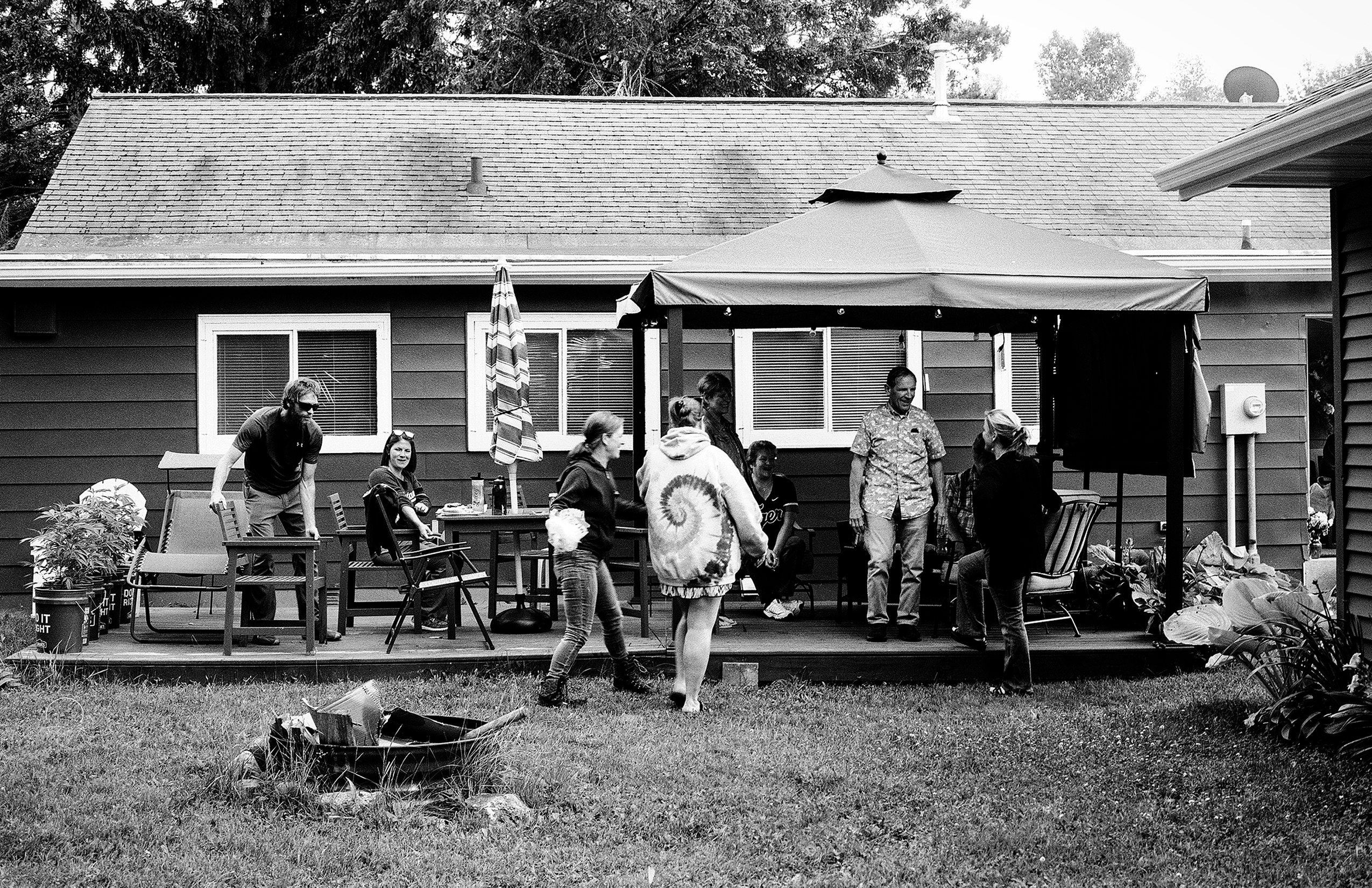 Family gathering on backyard deck with canopy tent people socializing in casual summer attire cottage home