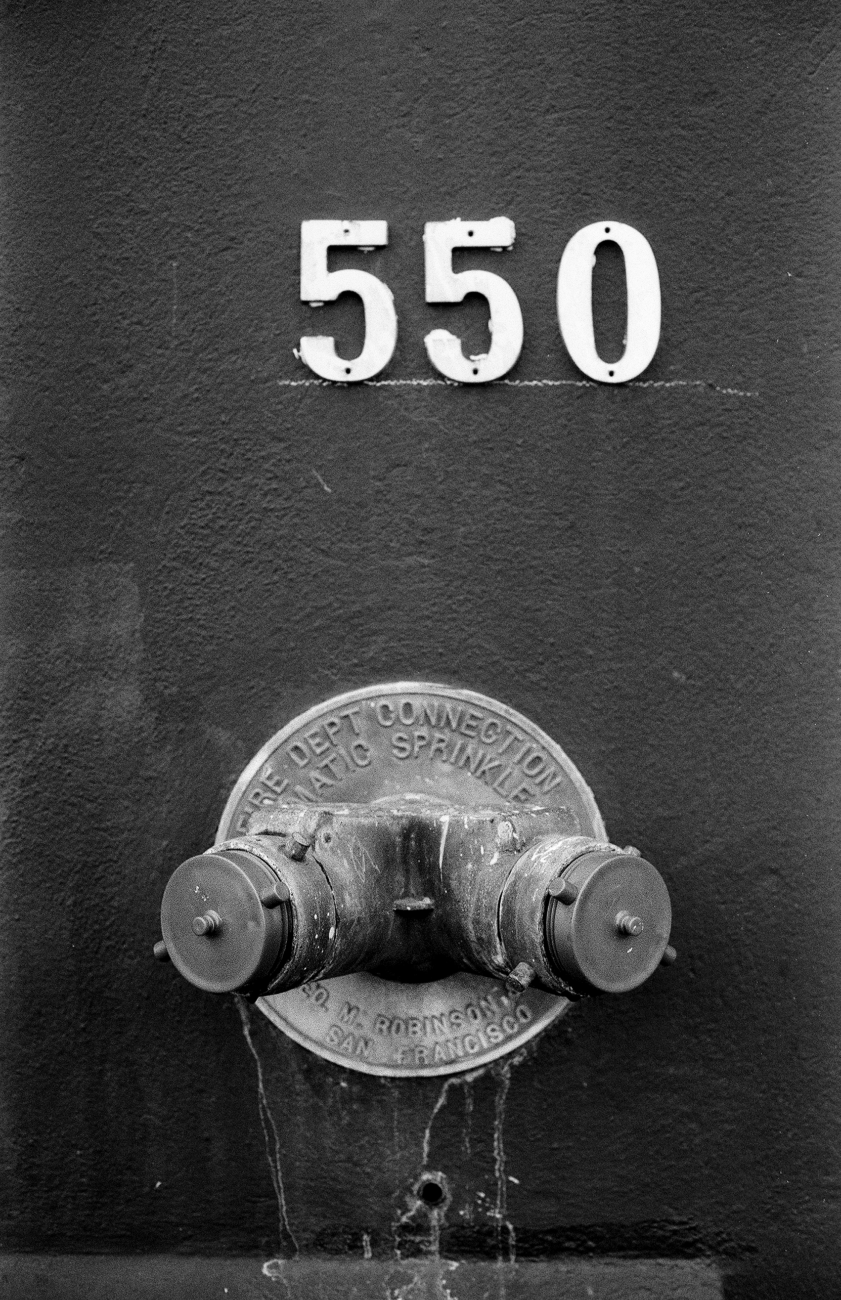 Fire department sprinkler connection mechanism with address number 550 and ornamental perforated metalwork on weathered concrete