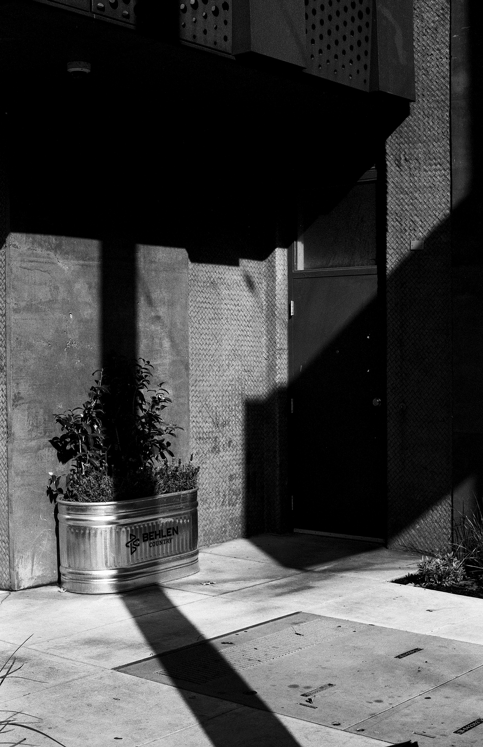 Dramatic shadow composition with angular sunlight across concrete alley featuring weathered metal planters and perforated architectural details