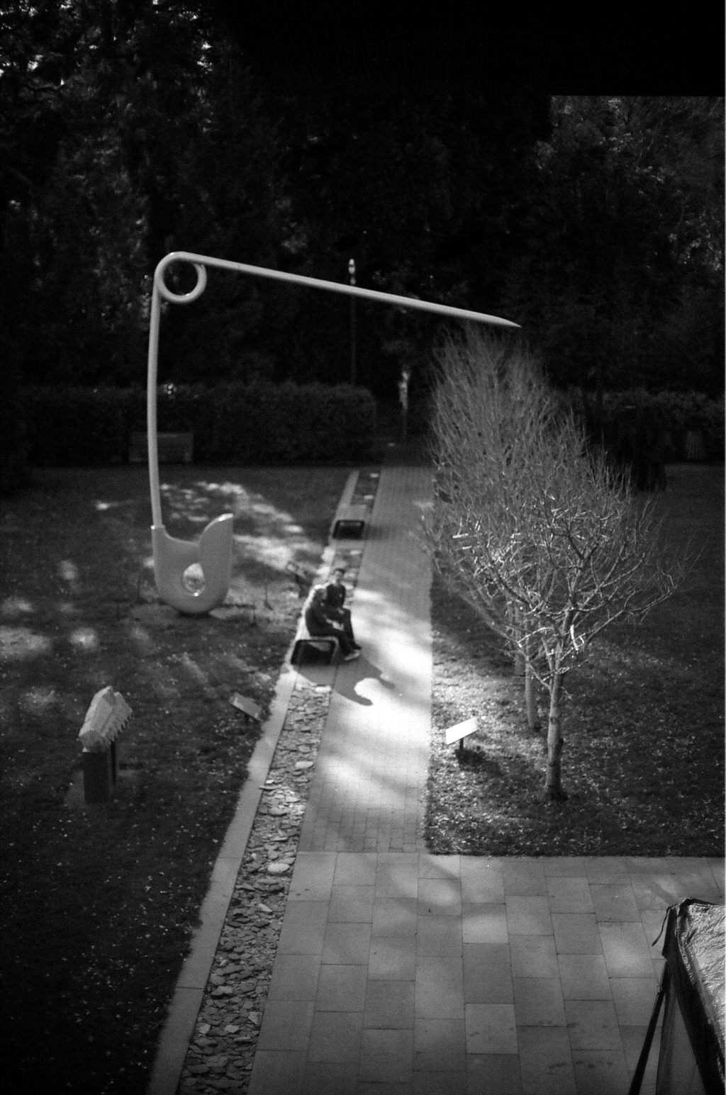 Modern sculptural art installation in park with curved metal form and trees
