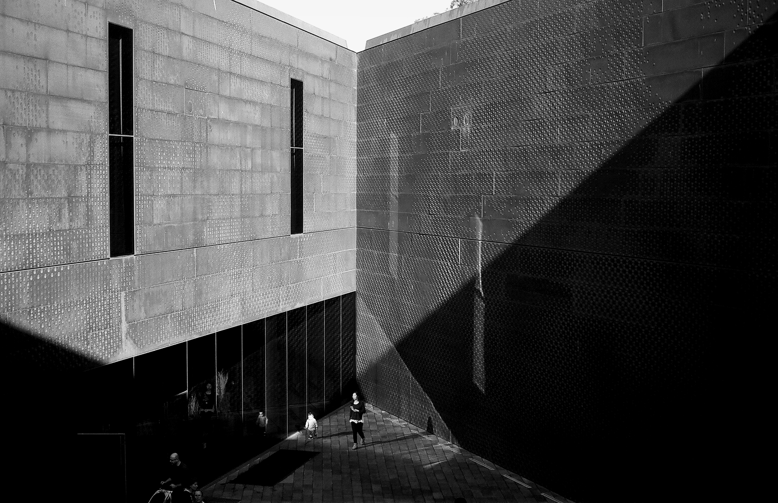 De Young Museum perforated copper facade with people walking in courtyard dramatic angular shadows and modernist architecture