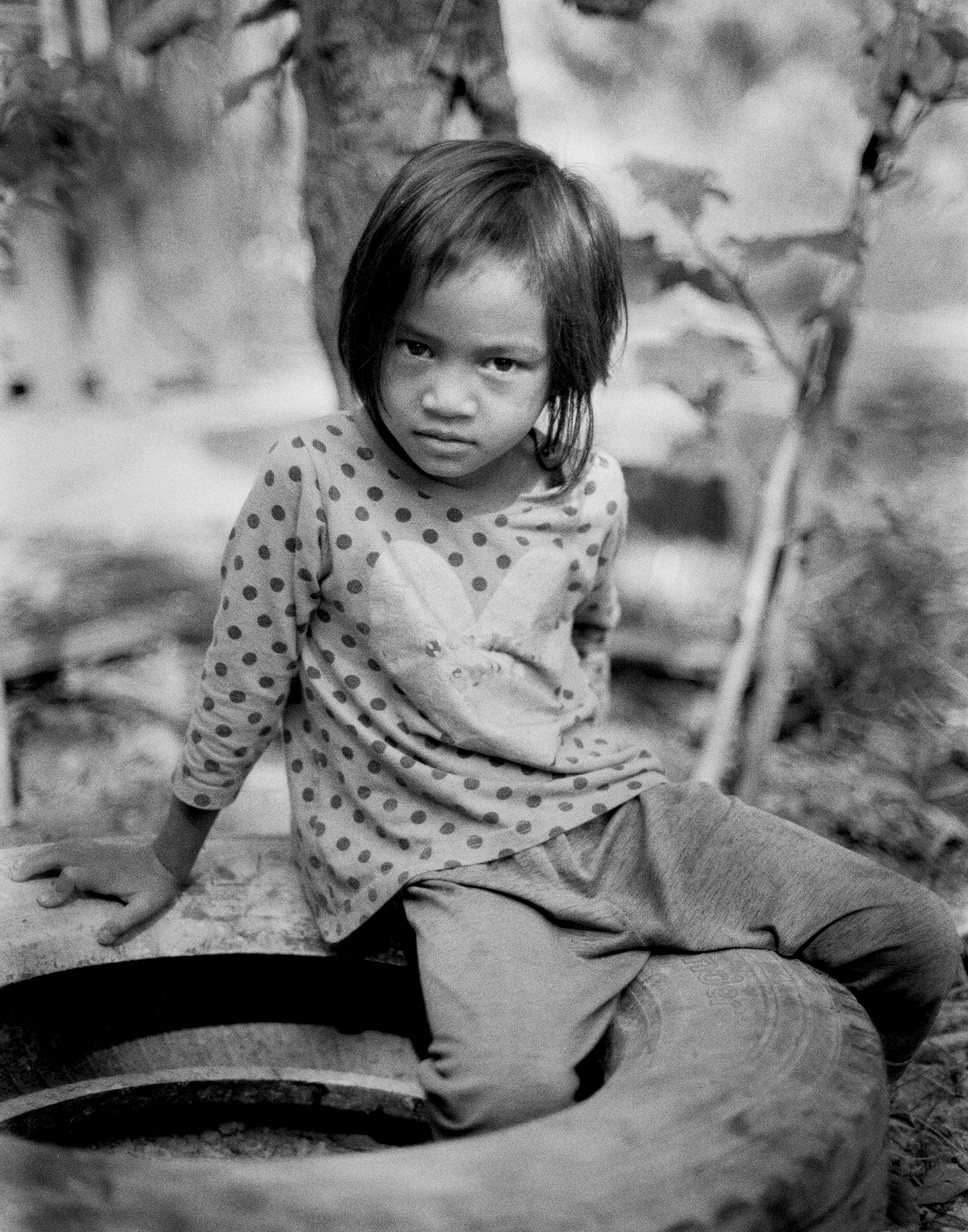 Portrait of young Cambodian girl in patterned shirt seated outdoors with direct gaze