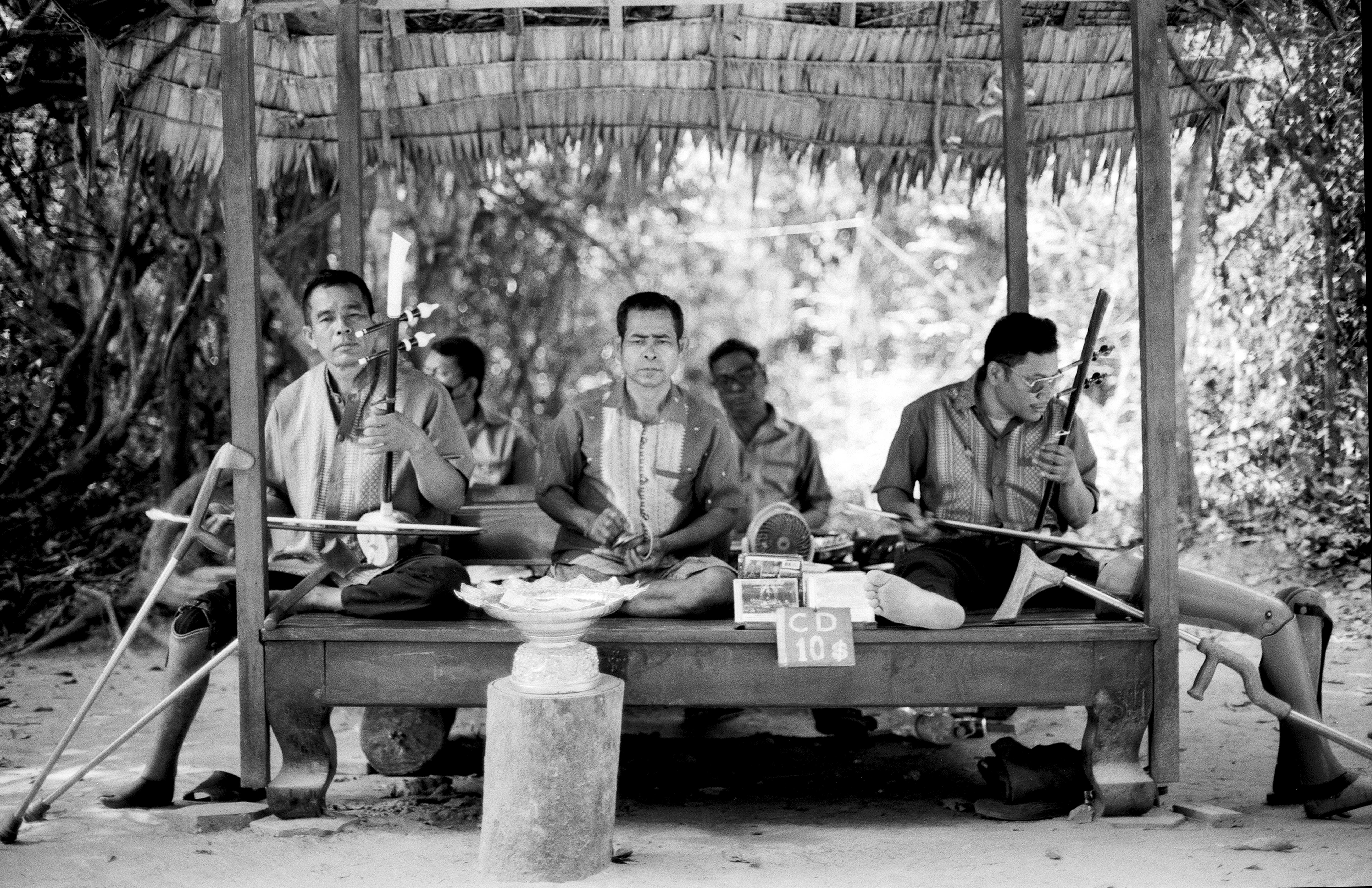 Musicians in traditional dress playing instruments outdoors under thatched pavilion shelter