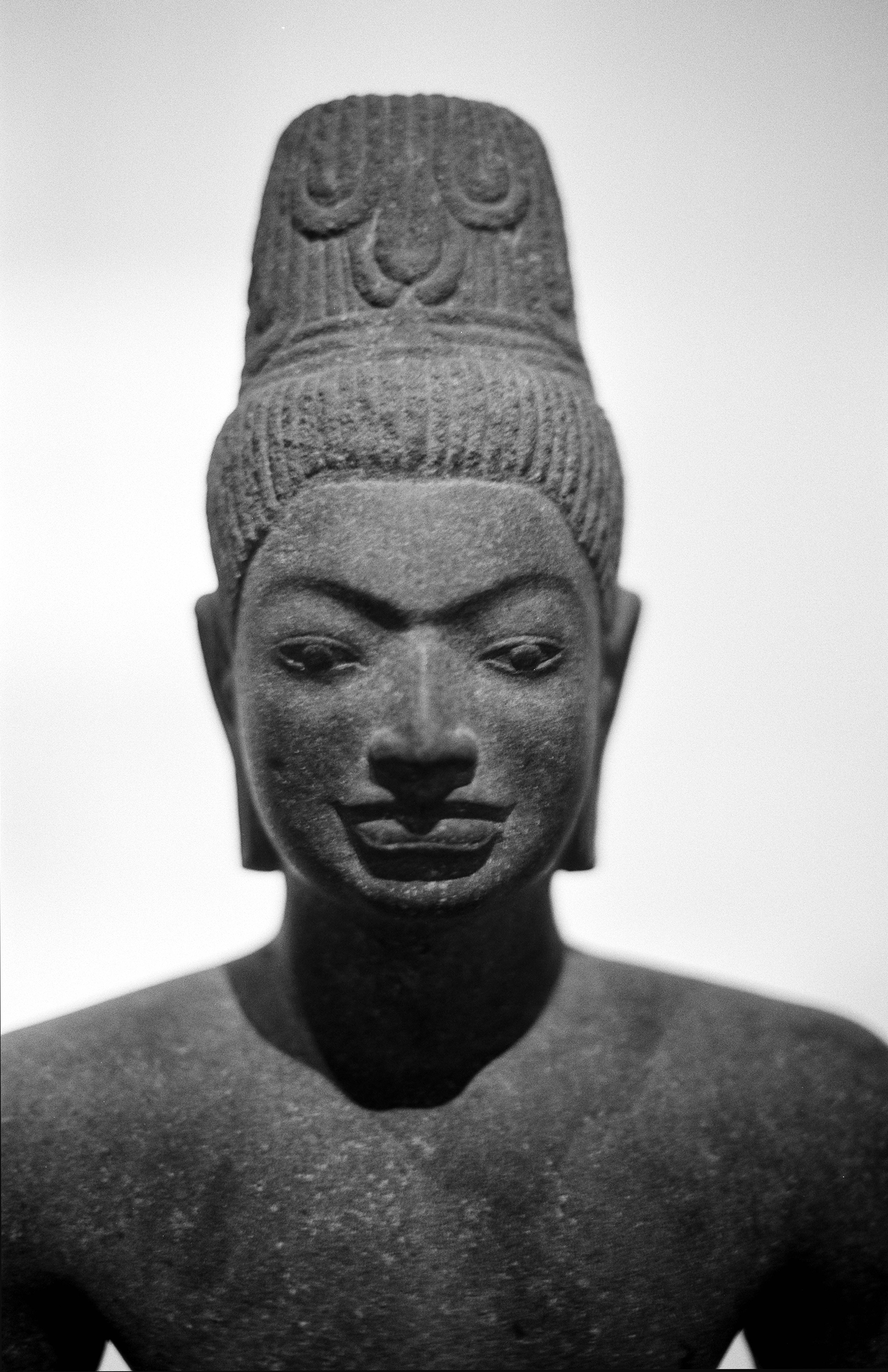 Close-up portrait of Khmer stone sculpture head with elaborate headdress against white background