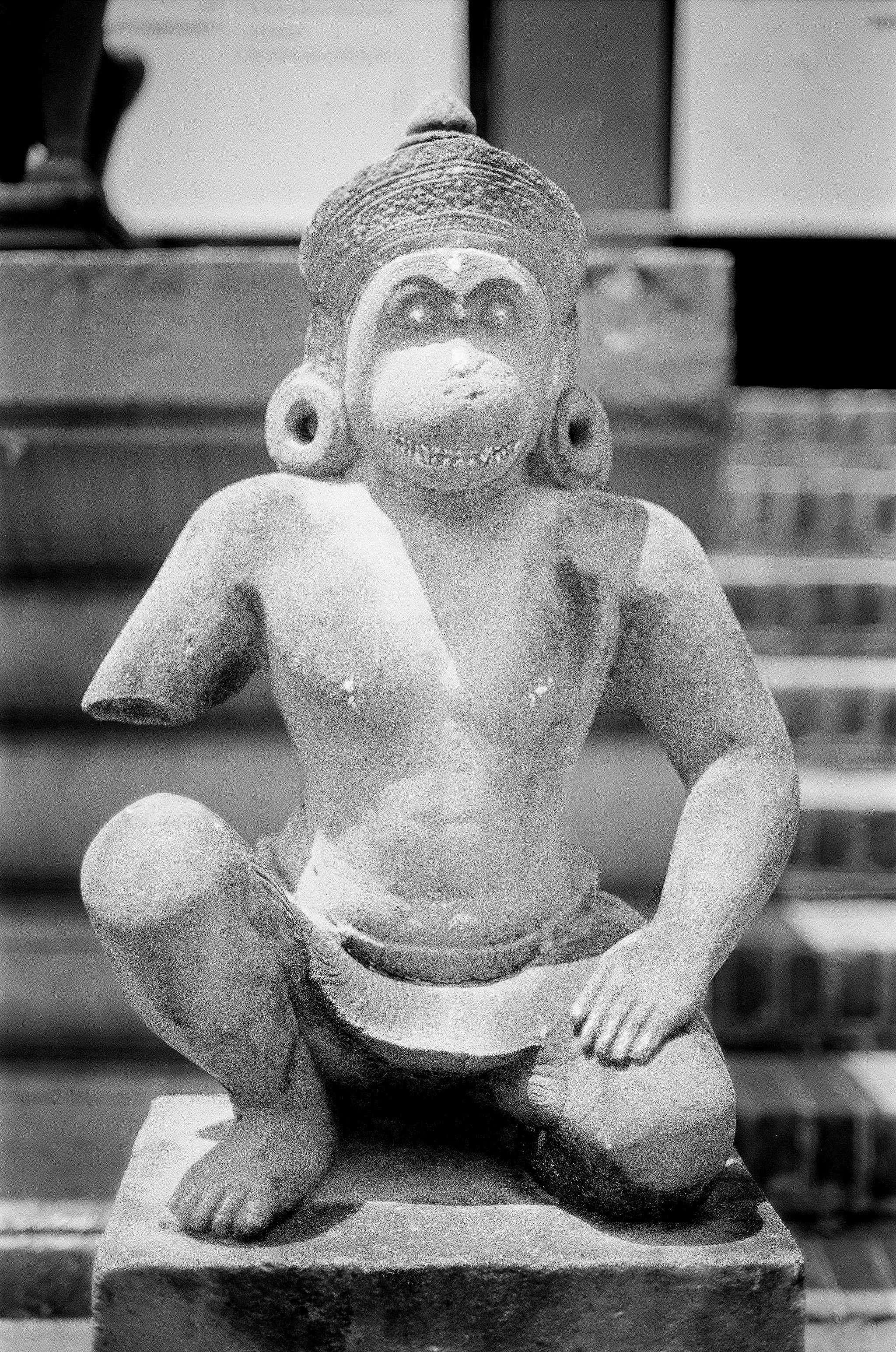 Stone monkey guardian sculpture with ornate headdress in meditation pose at temple ruins
