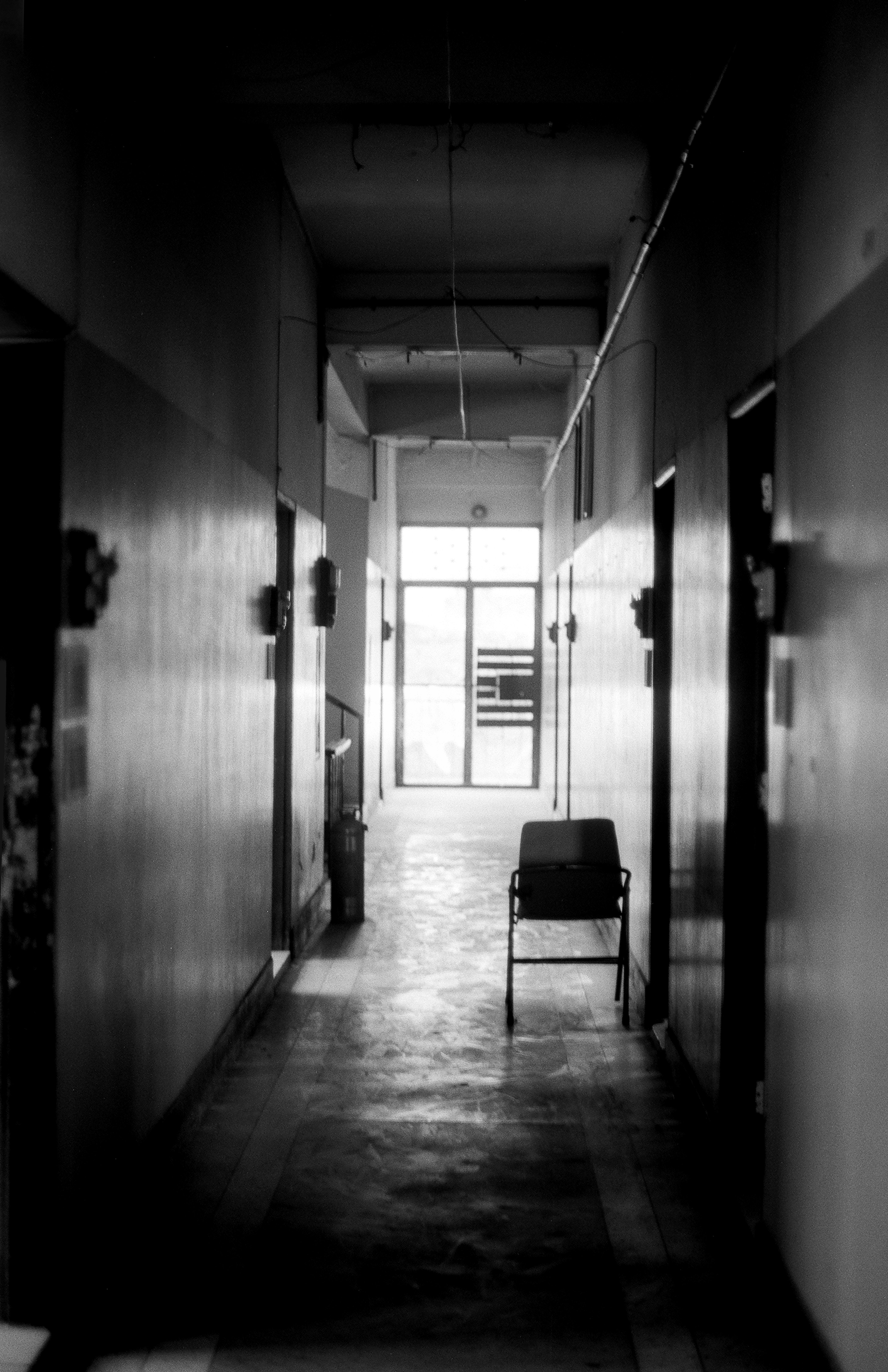 Atmospheric hallway with single chair and bright window at end creating dramatic light and shadow