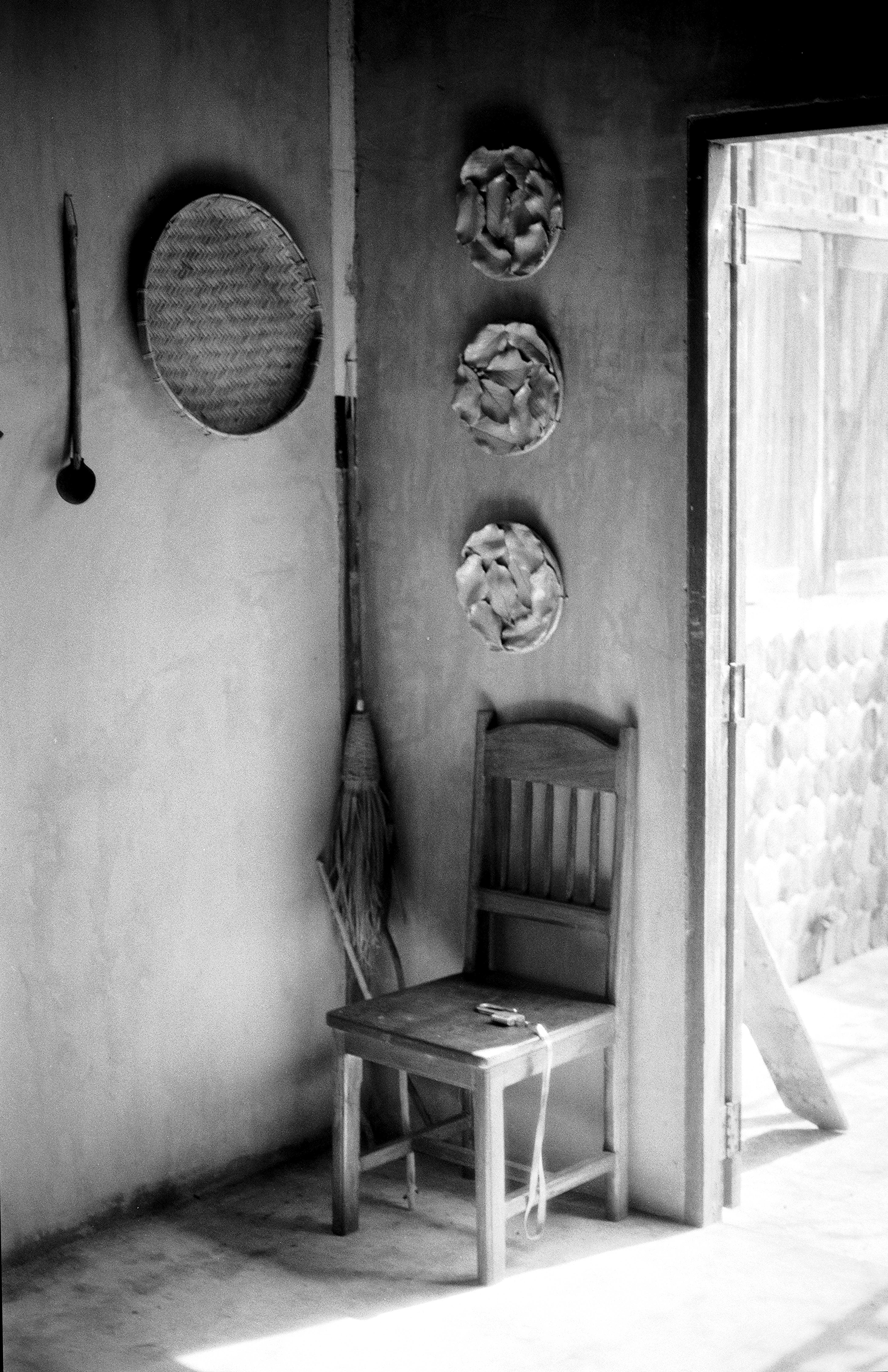 Rural Thai interior with wooden chair woven baskets ladle and traditional items on concrete wall near doorway