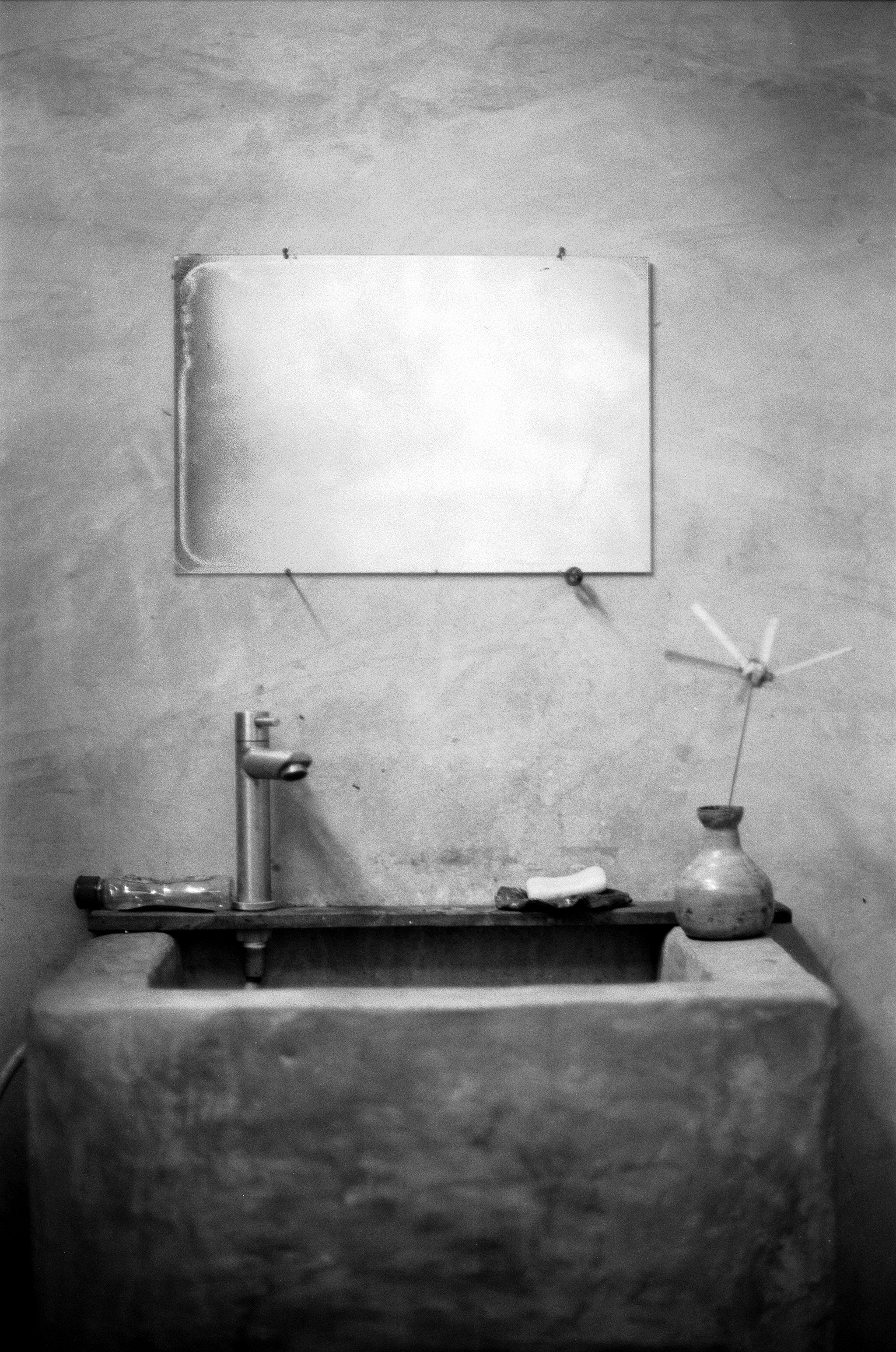 Simple washbasin with mirror faucet and ceramic vase with dried flower in minimalist concrete bathroom