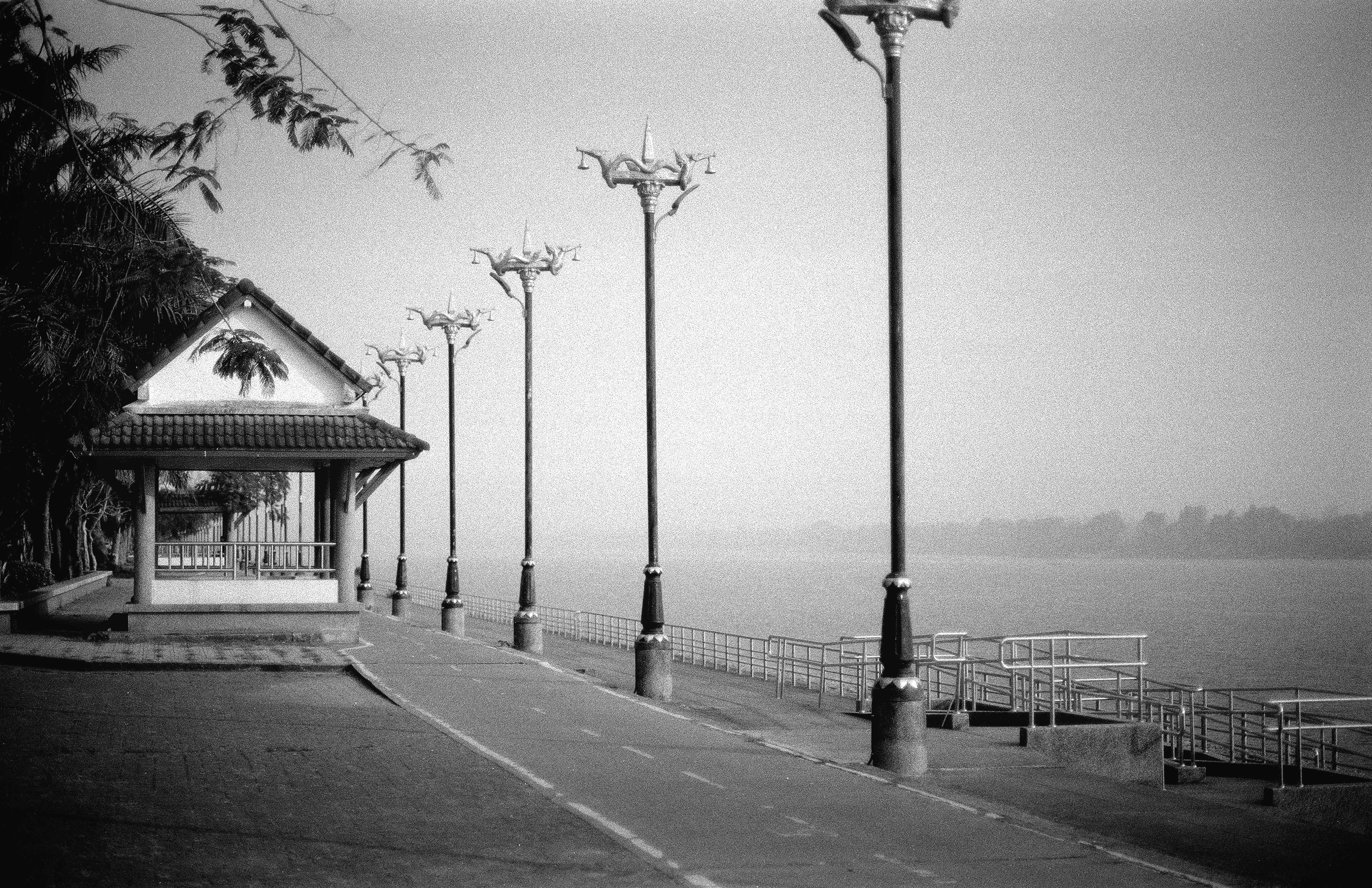 Riverside promenade with ornate traditional lampposts and pavilion along Mekong River in misty morning light