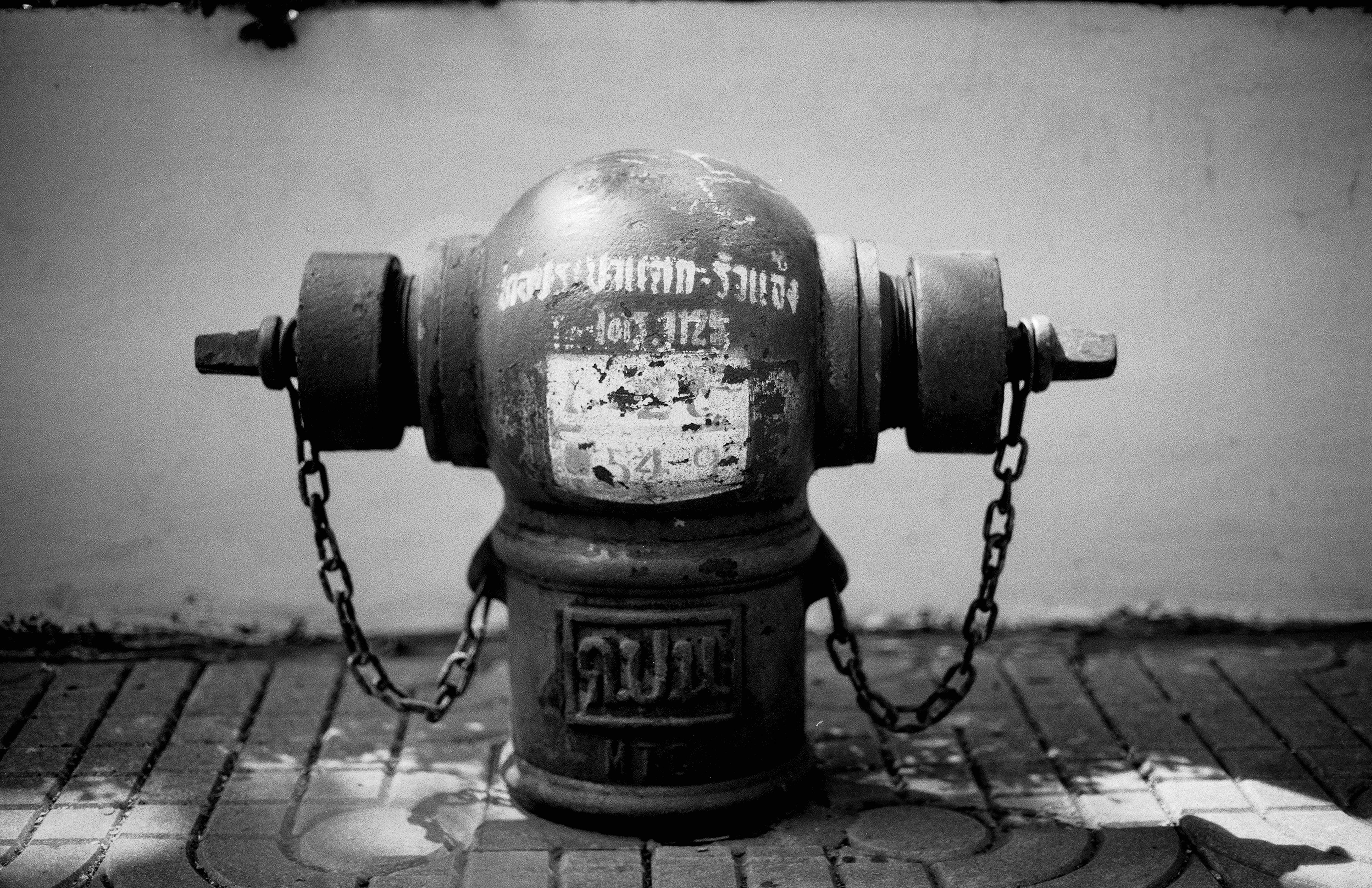 Fire hydrant with Thai script and chains on brick pavement in symmetrical frontal composition
