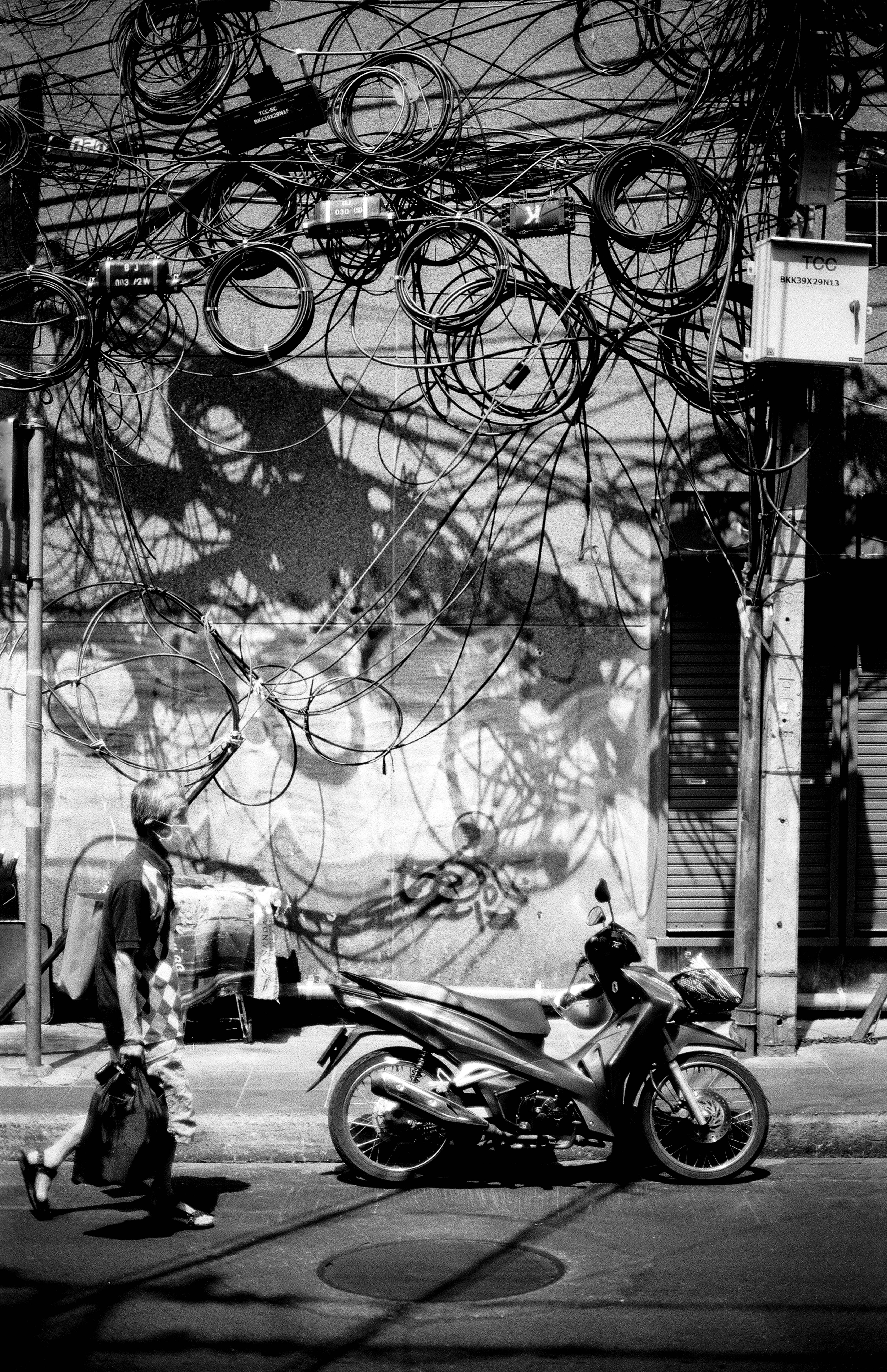 Motorcyclist passing beneath chaotic tangle of electrical wires with Starbucks sign in Bangkok street scene