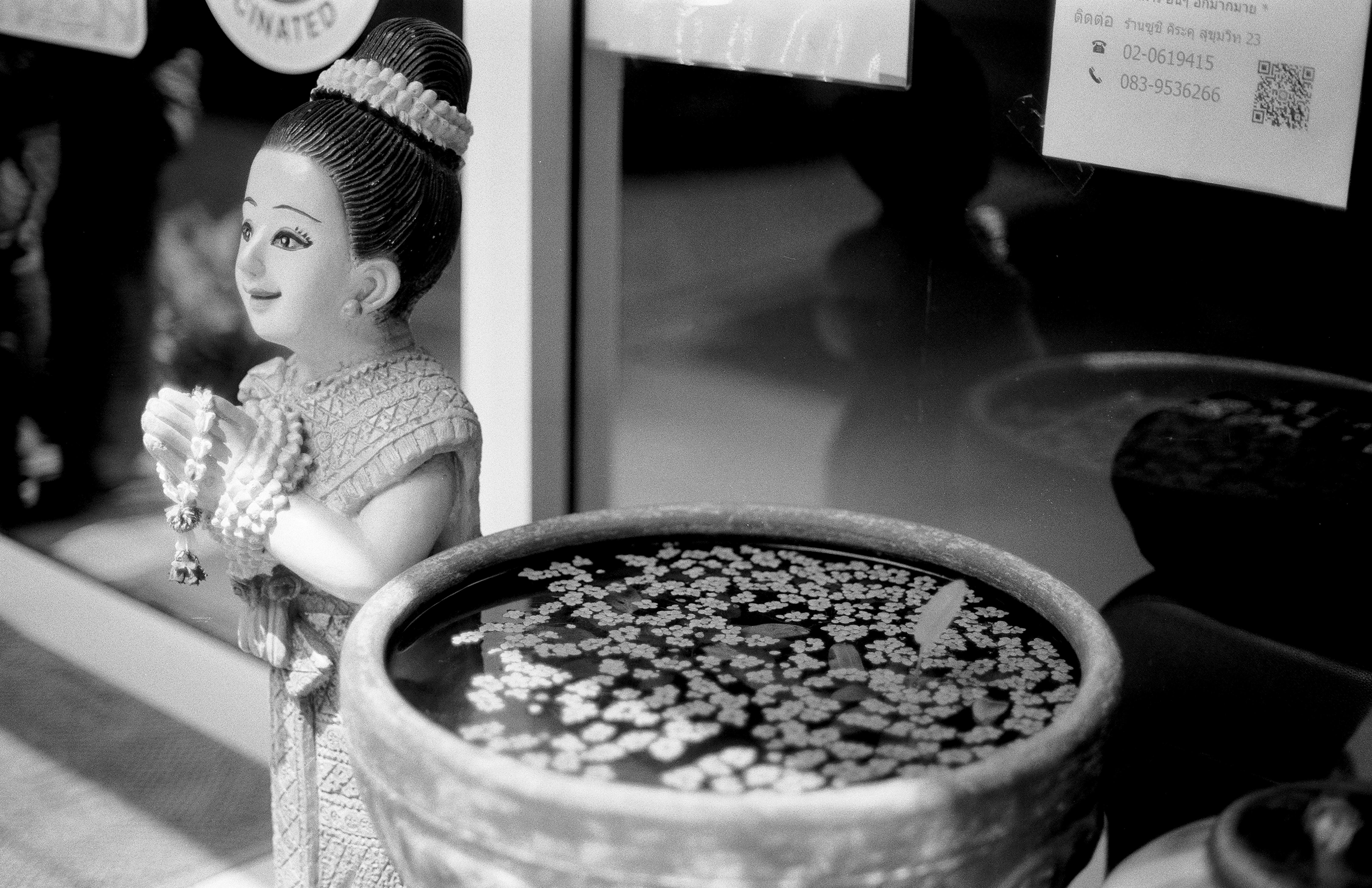 Traditional Thai figurine in wai greeting pose next to water basin with floating jasmine flowers