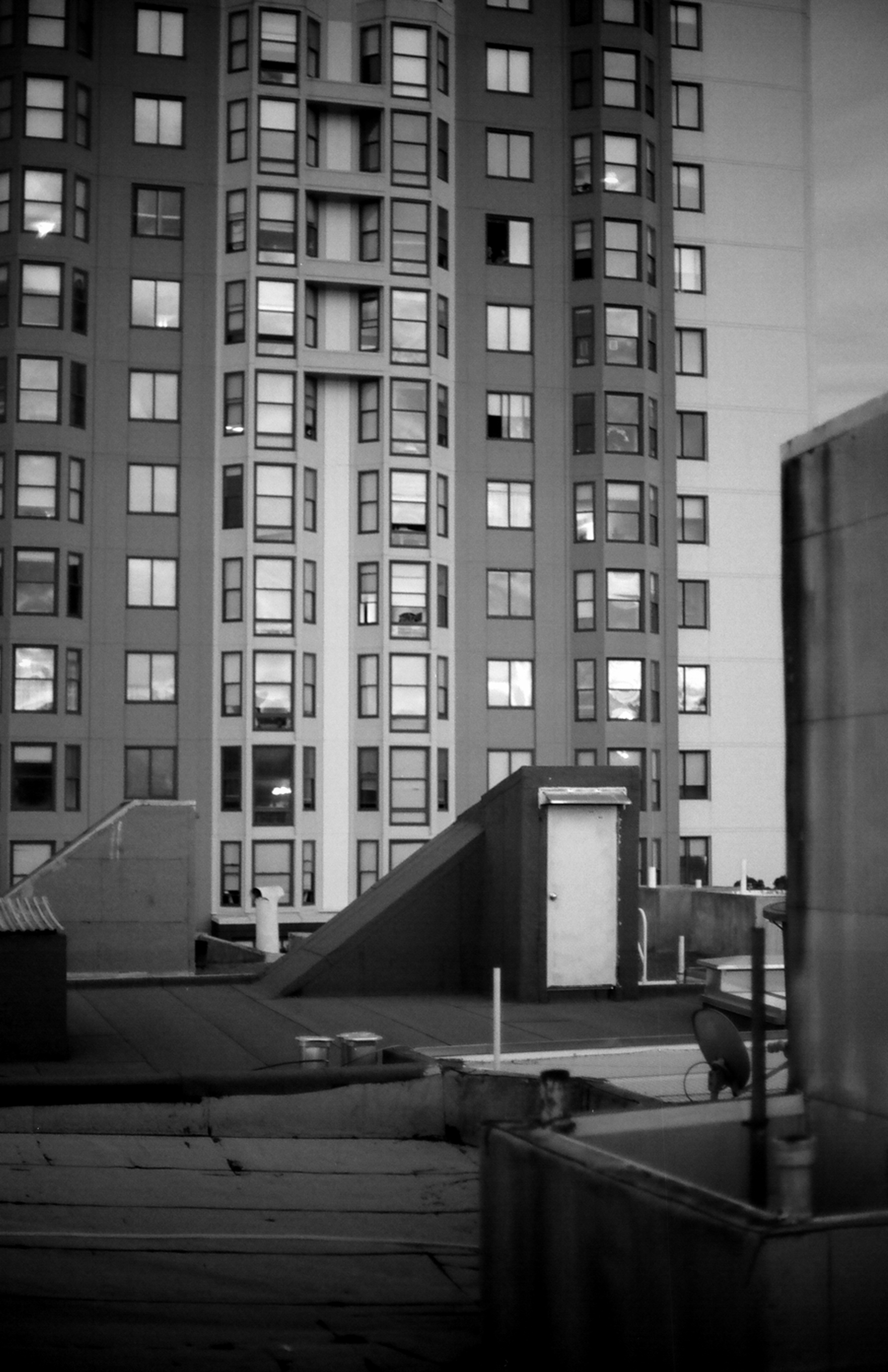 Brutalist high-rise residential building with repetitive window grid pattern and rooftop utility structures photographed from street level
