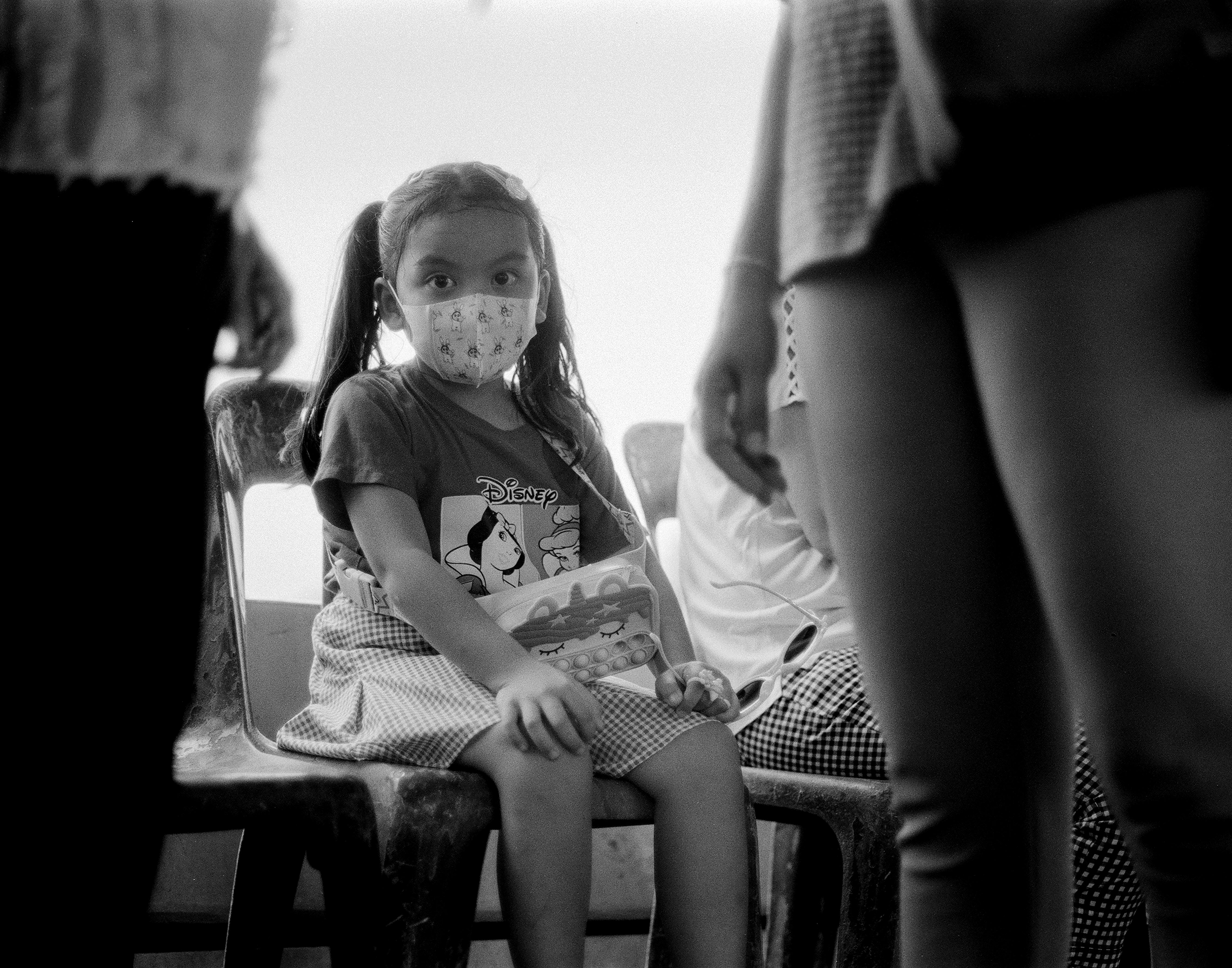 Young Thai girl with pigtails wearing face mask and Disney princess shirt seated holding toy looking at camera