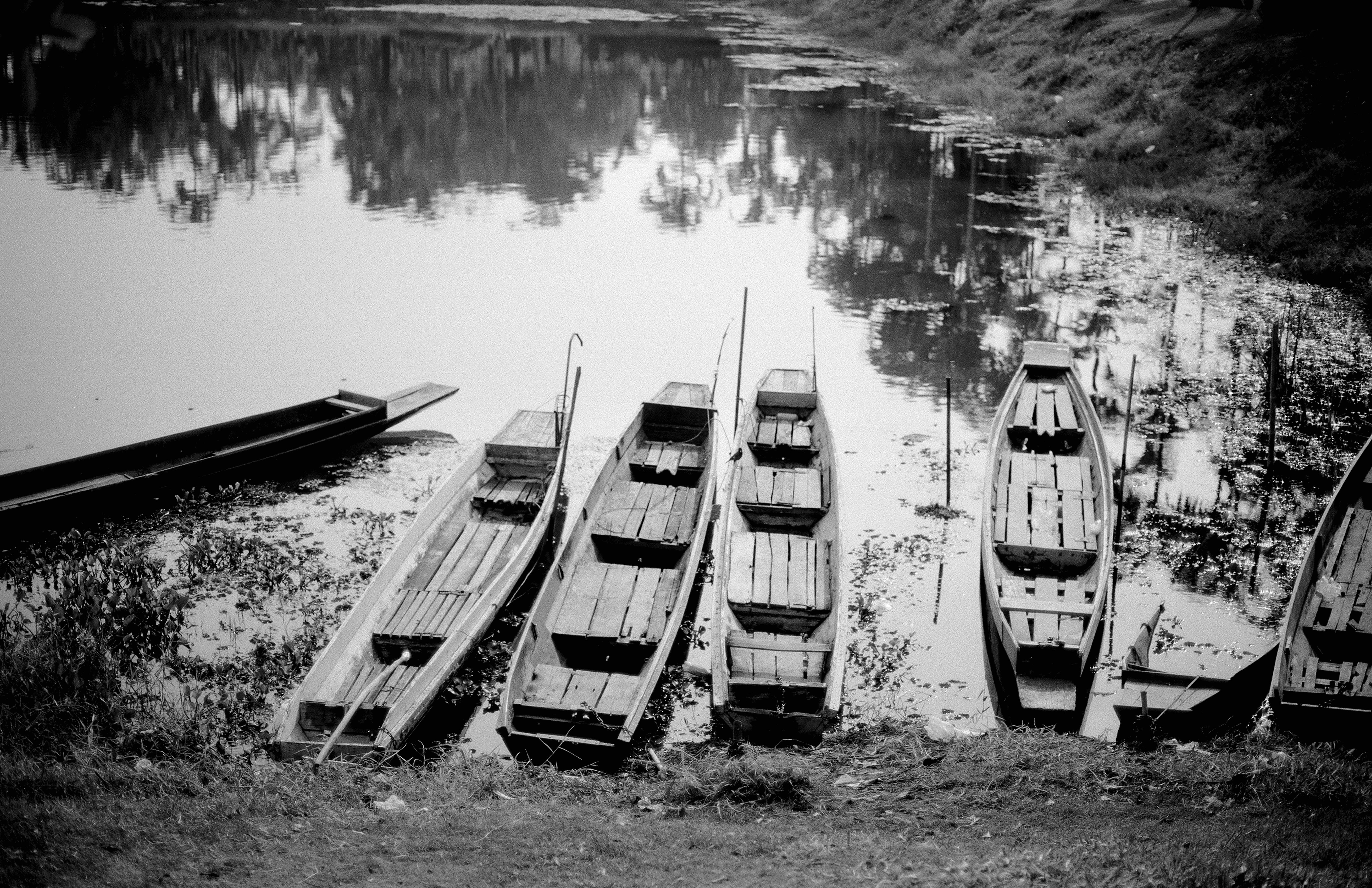 Traditional wooden boats moored along riverbank with beautiful reflections in calm water