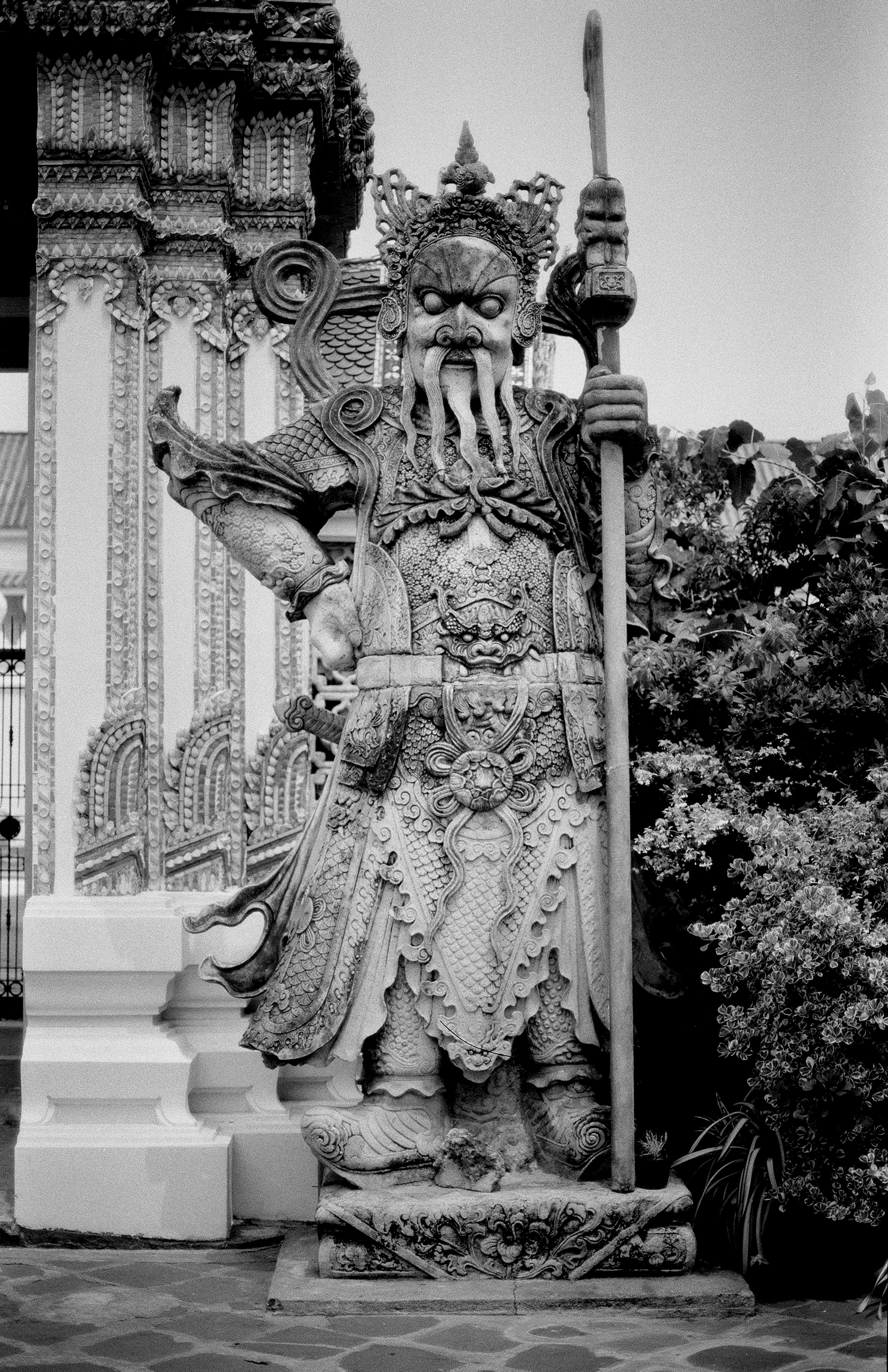Ornate Chinese guardian warrior statue holding staff at Thai temple with intricate dragon and demon carvings