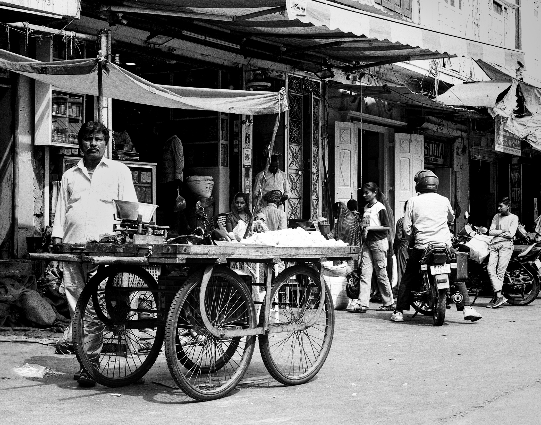 Black and white street food vendor serving customers from push cart with storefront awnings background