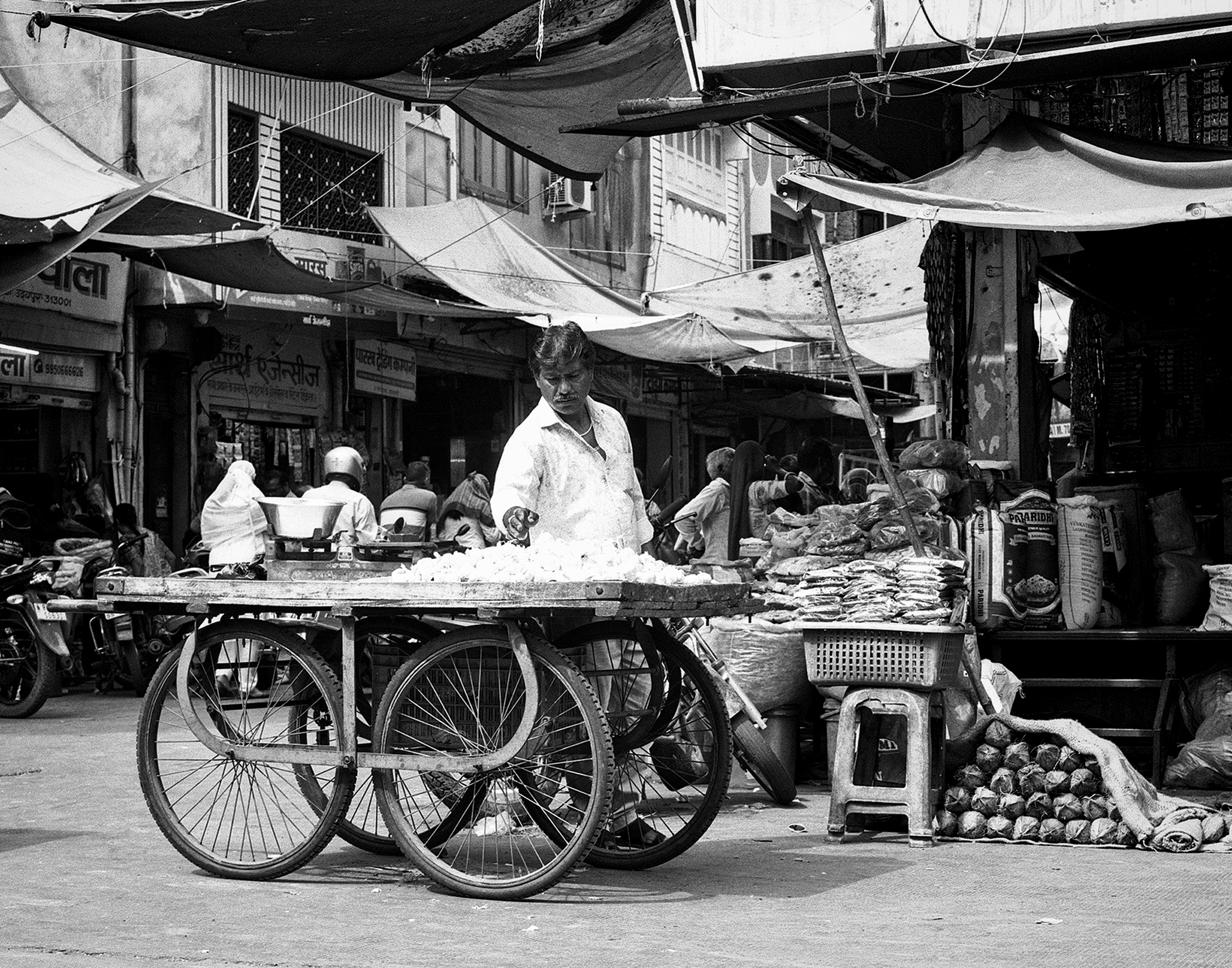 Black and white street food vendor with hand-pulled cart serving customers under canvas shade