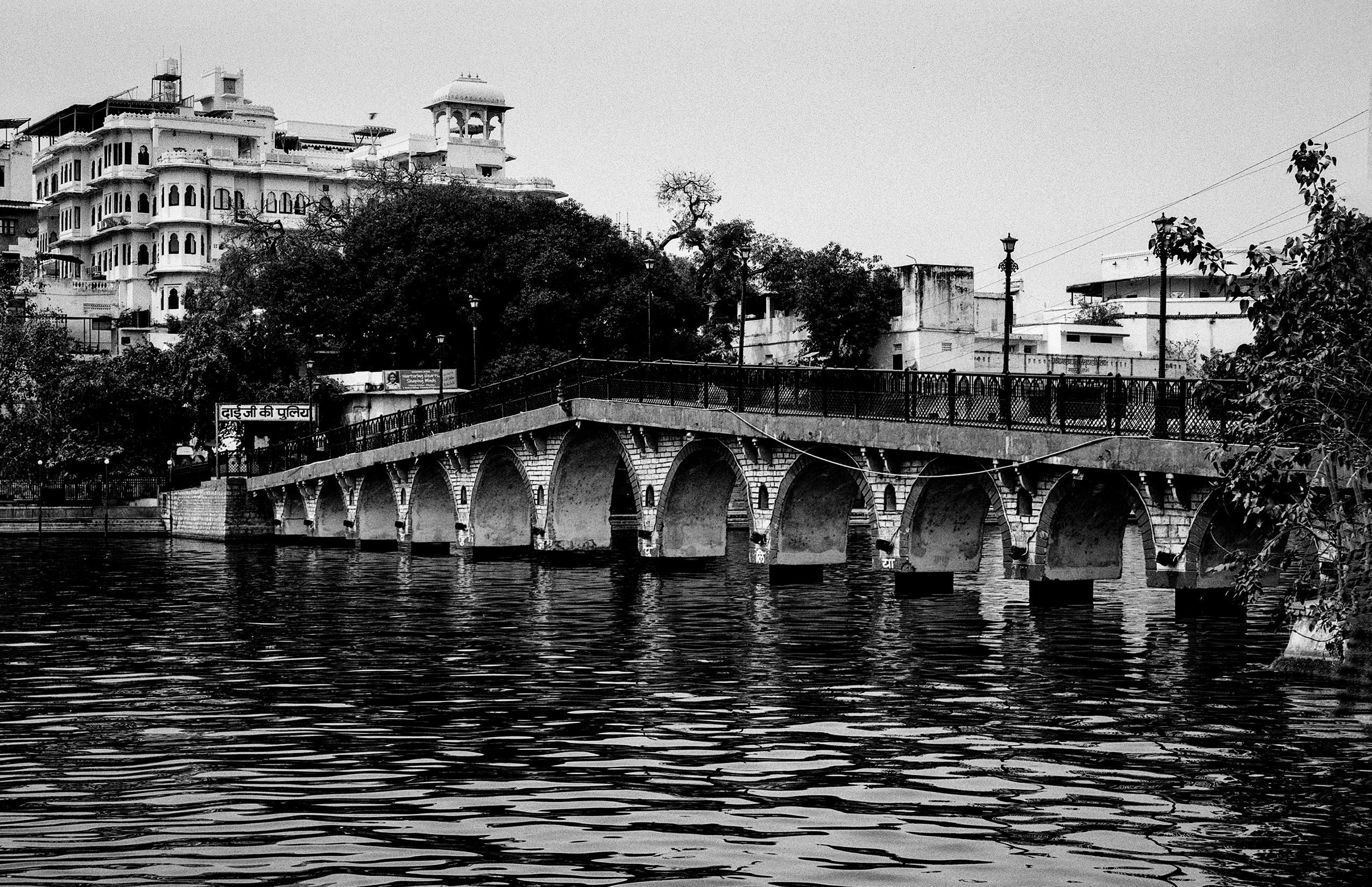 Black and white historic stone arch bridge spanning river with white palace buildings hills beyond