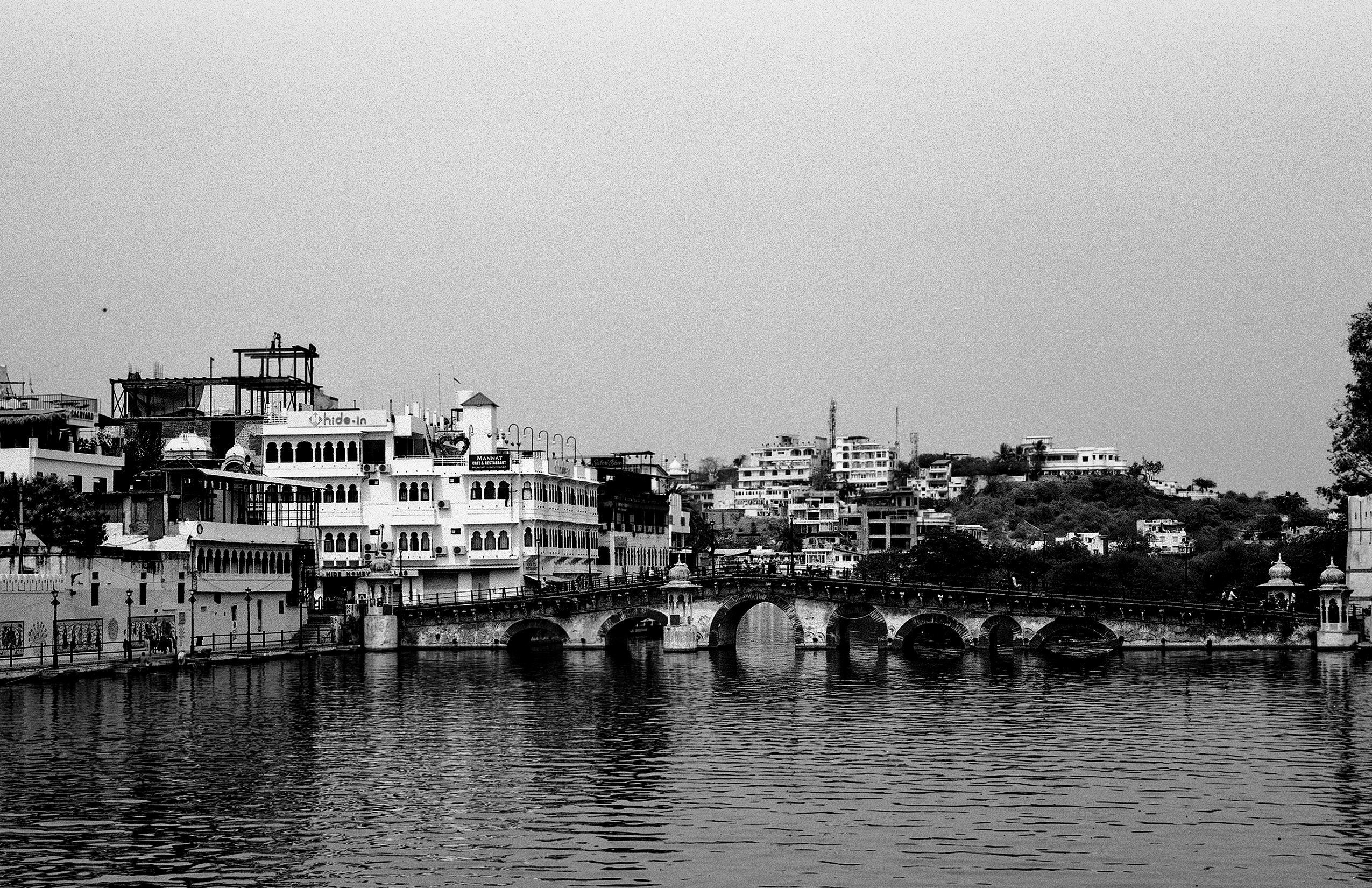 Black and white Udaipur waterfront with grand palace architecture reflected in water and ancient stone bridge