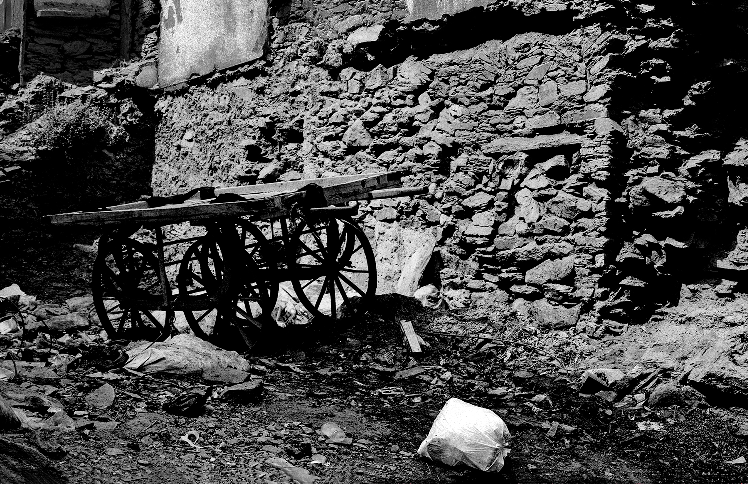 Black and white abandoned wooden cart with large wheels against rocky hillside weathered ruins