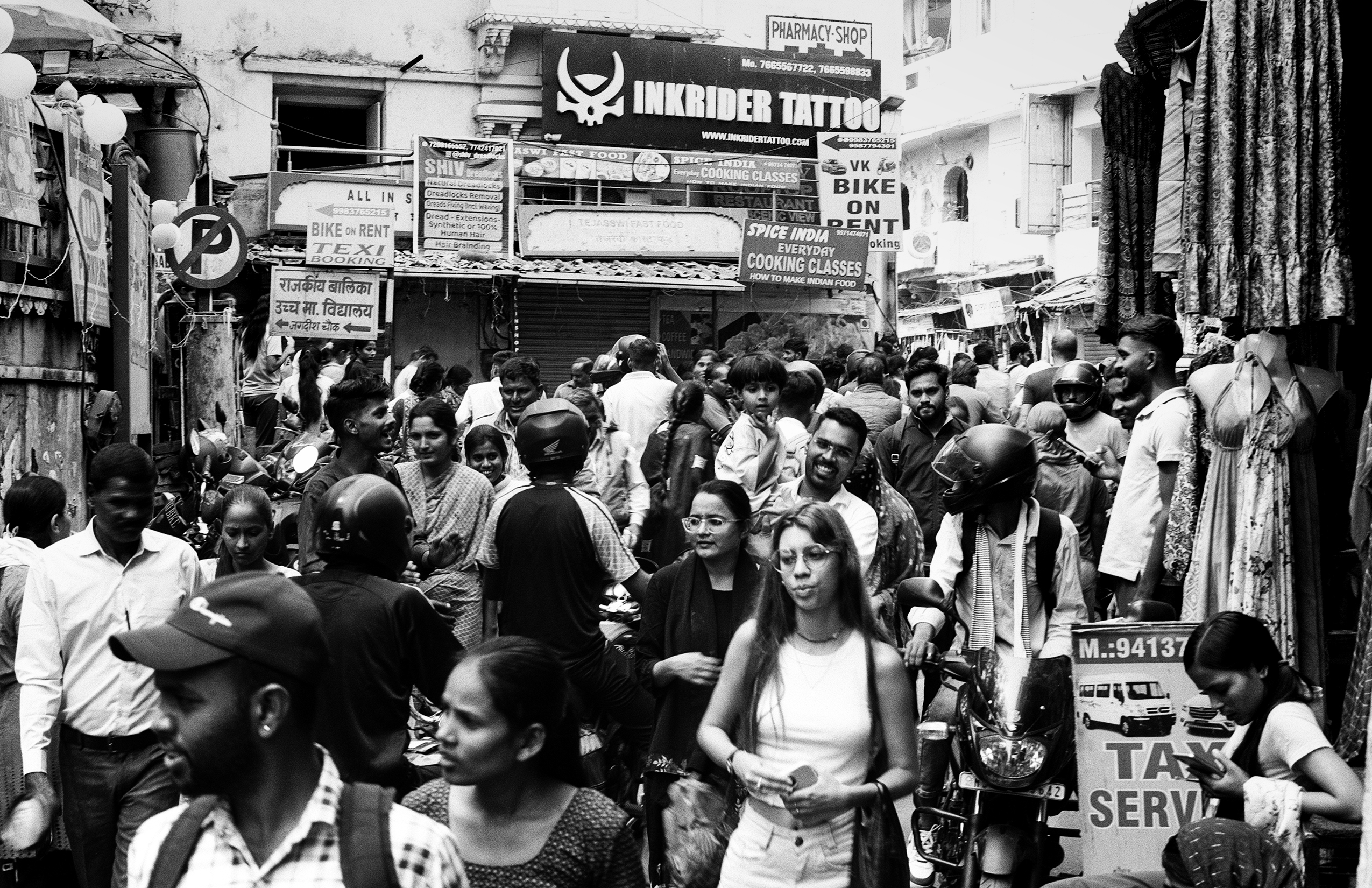 Black and white crowded street market scene with shops motorcycles and busy pedestrian activity