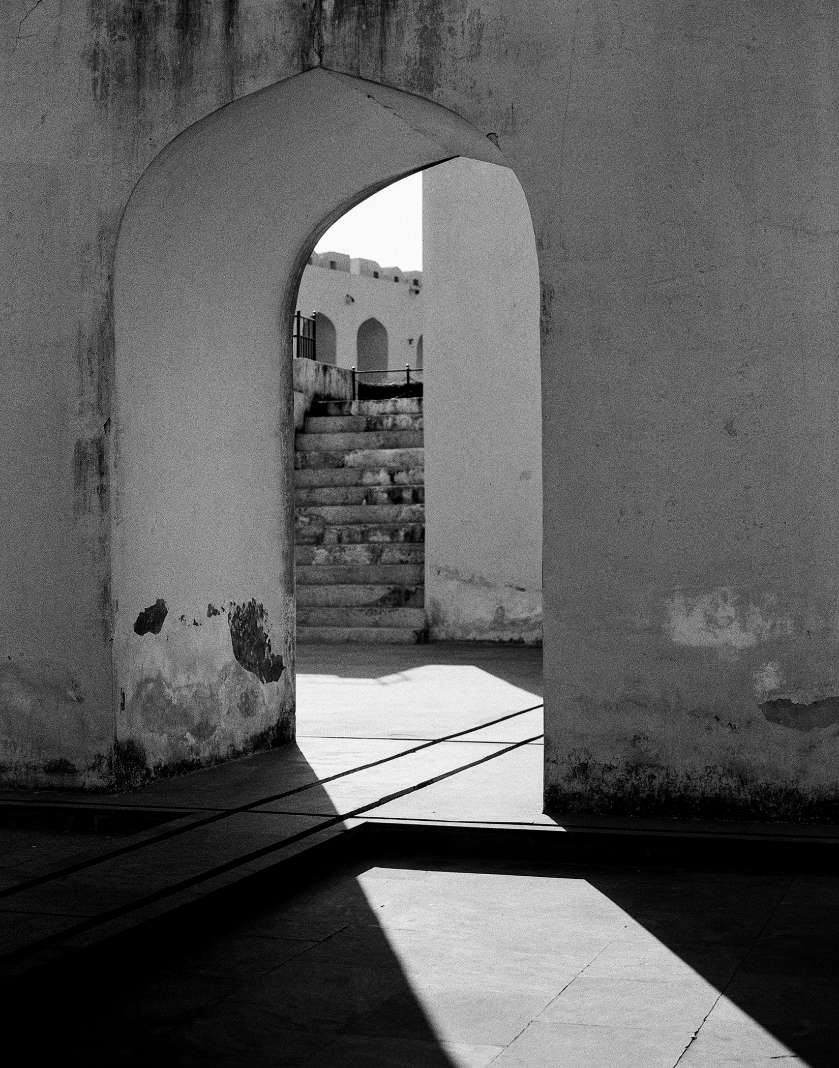 Black and white archway passage with light streaming in and stone stairs leading upward