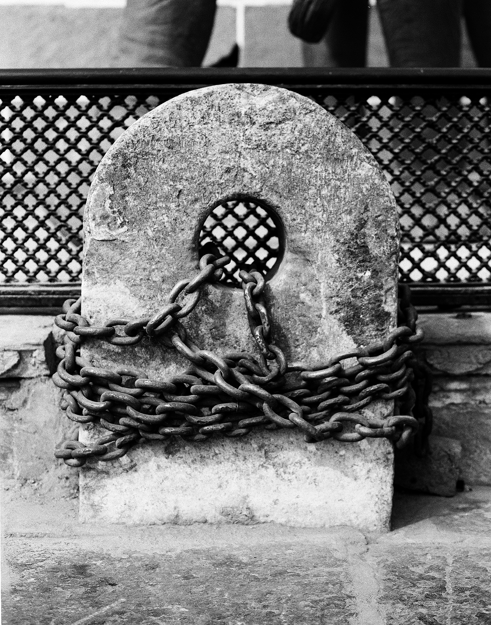 Black and white ancient stone wheel wrapped in heavy chains against lattice screen
