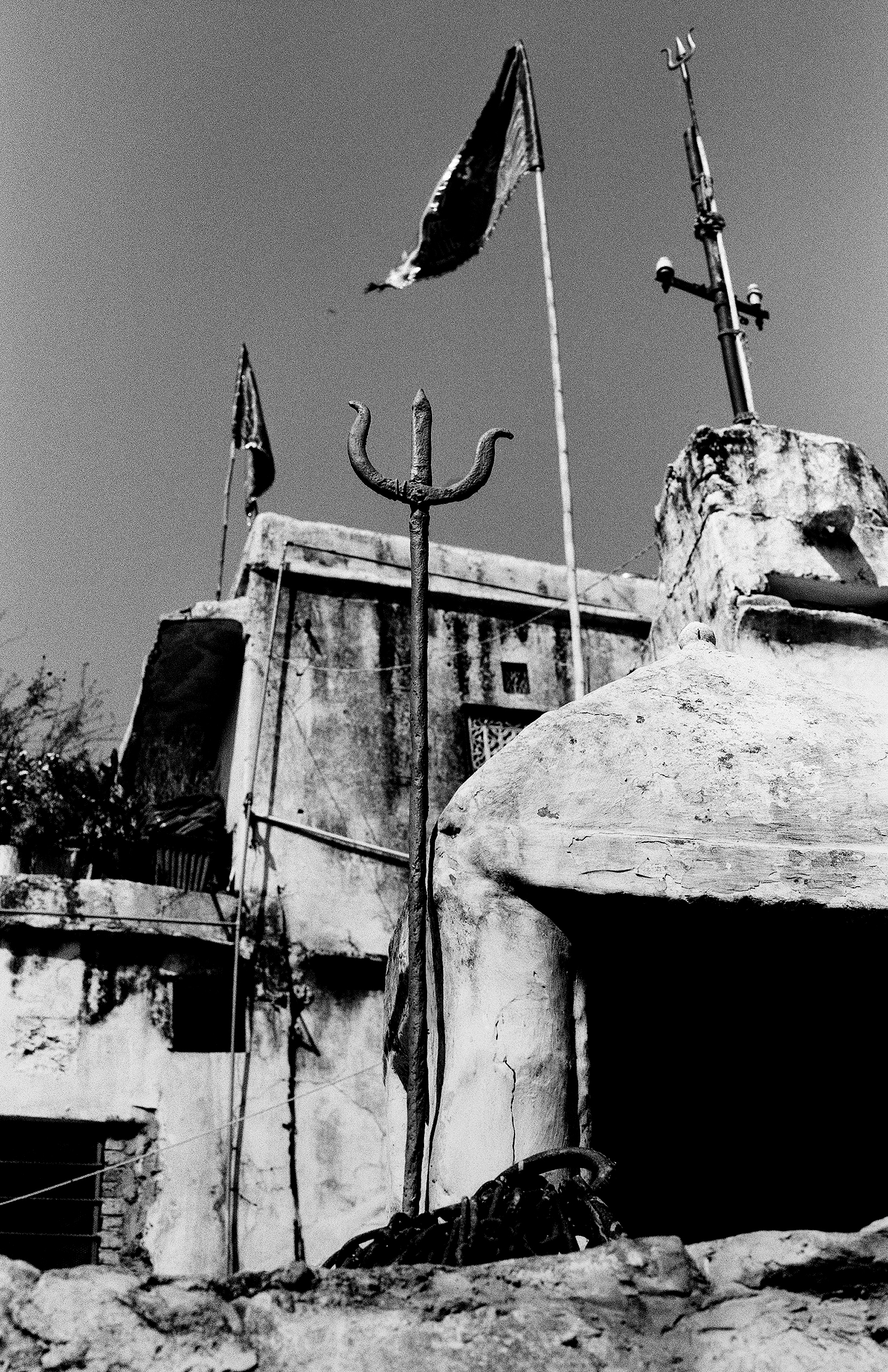 Black and white ceremonial trident and flags at temple entrance with weathered fort architecture background