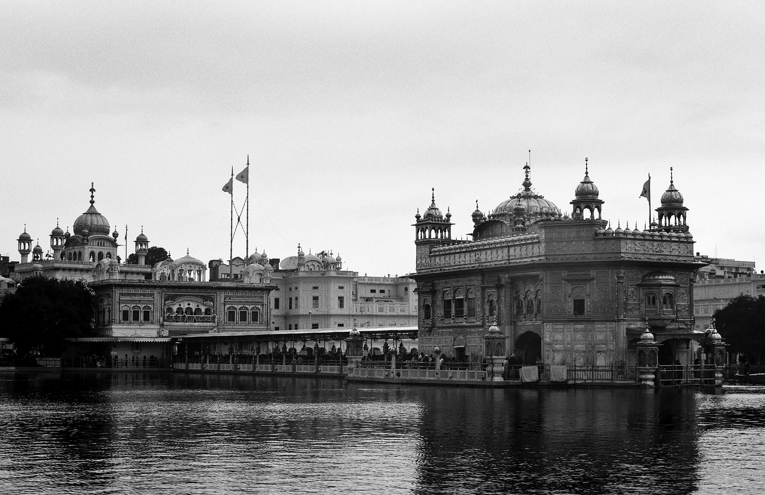 Black and white panoramic view of Amritsar Harmandir Sahib and Akal Takht with crowds and sacred pool at night