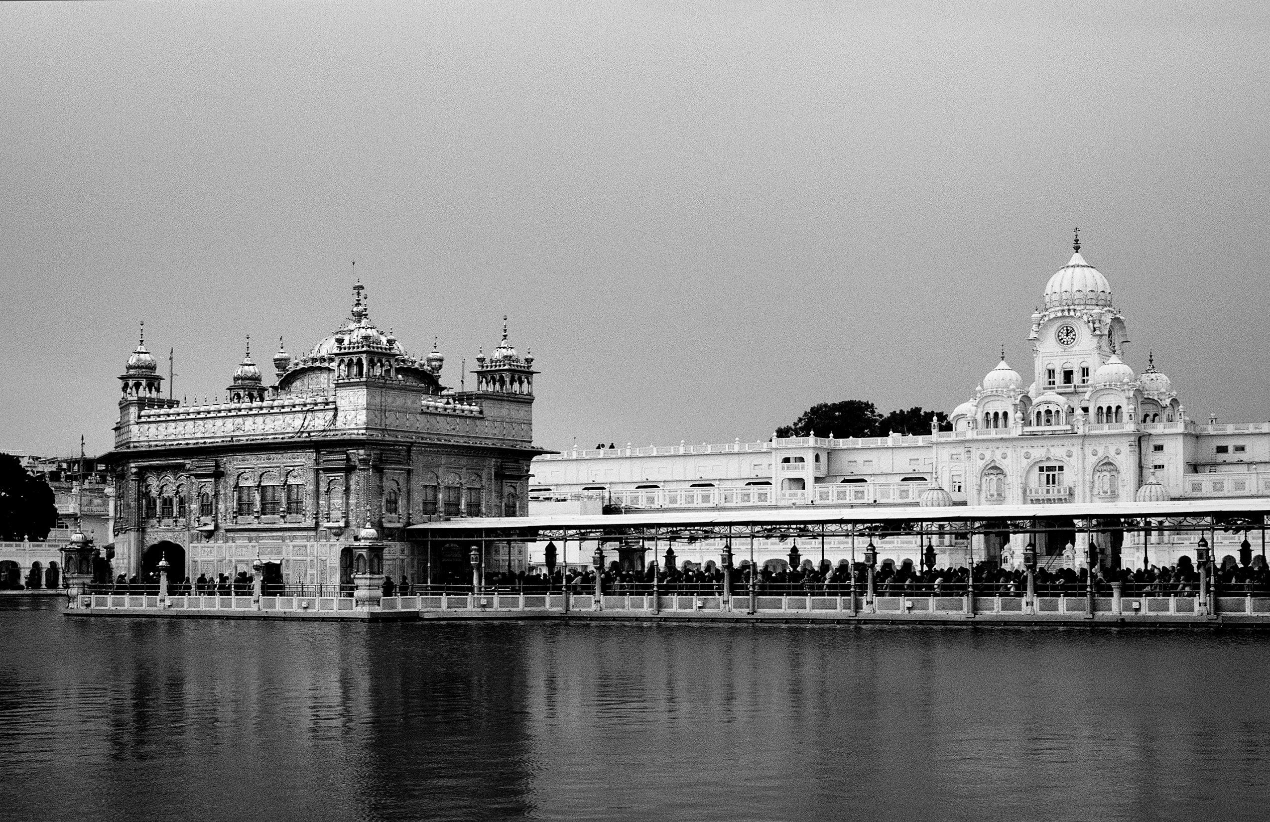 Black and white Golden Temple of Amritsar across sacred pool with pilgrims and ornate railing foreground