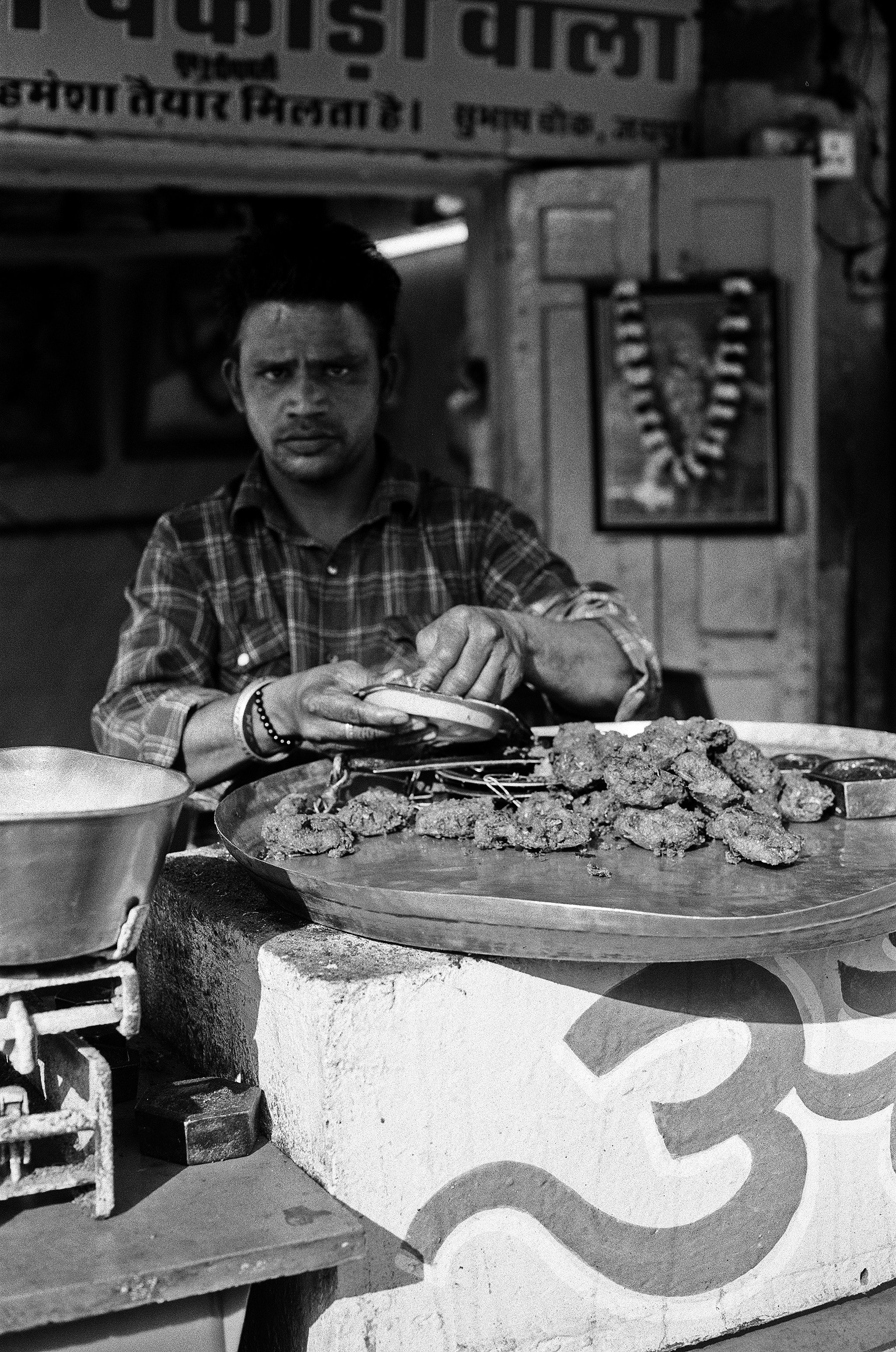 Black and white street food vendor preparing fried snacks pakoras on large metal platter wearing checkered shirt