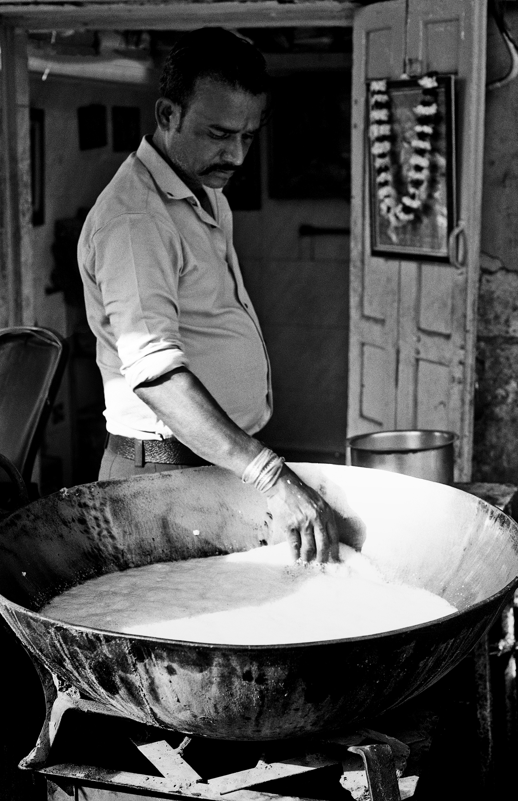 Black and white man in light shirt stirring large metal cooking vessel with water creating traditional dish
