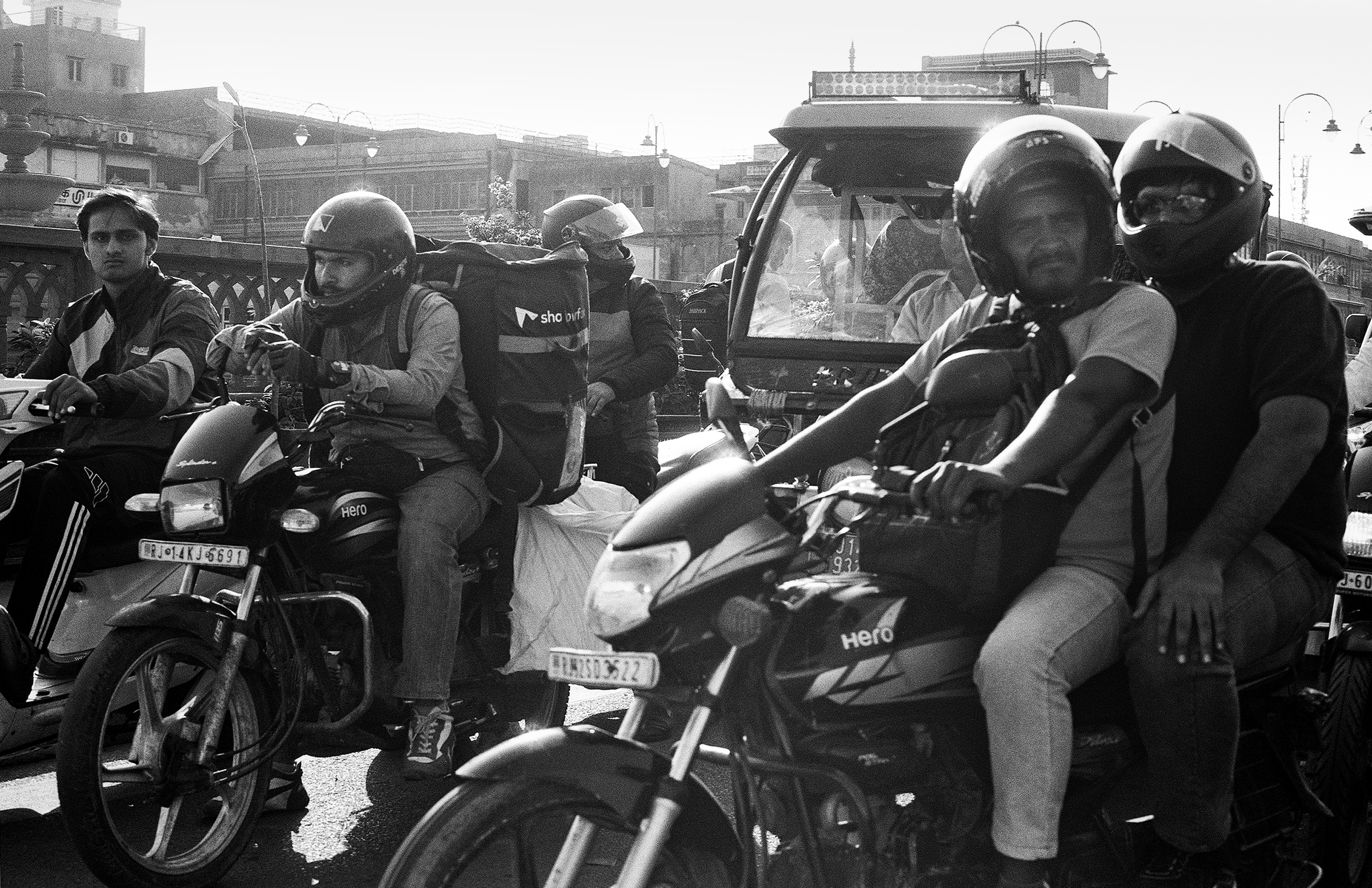 Black and white group of motorcycle taxi drivers with helmets gathered on city street with buildings background