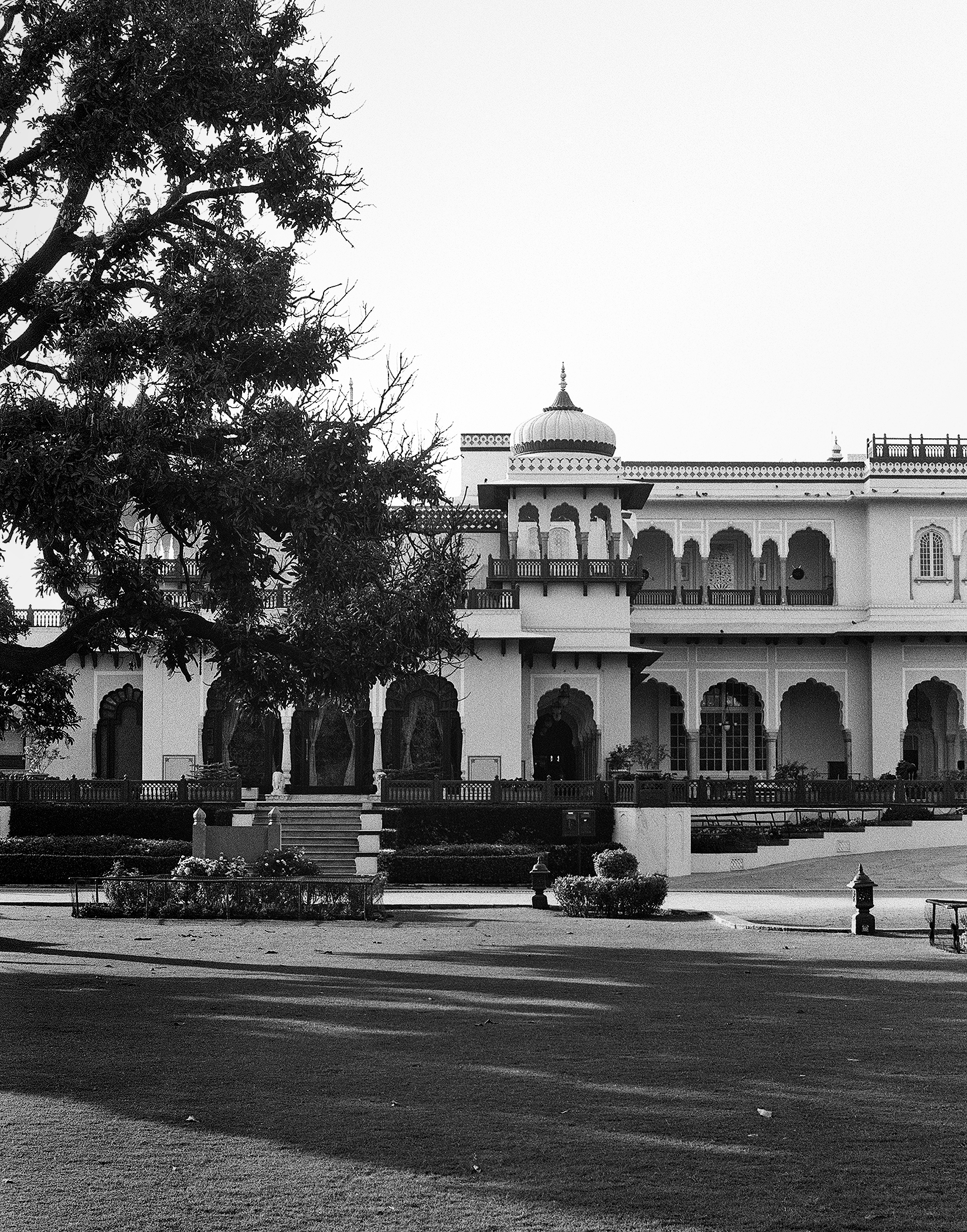 Black and white Jaipur palace exterior with domed architecture ornate railings arches and tree-framed courtyard