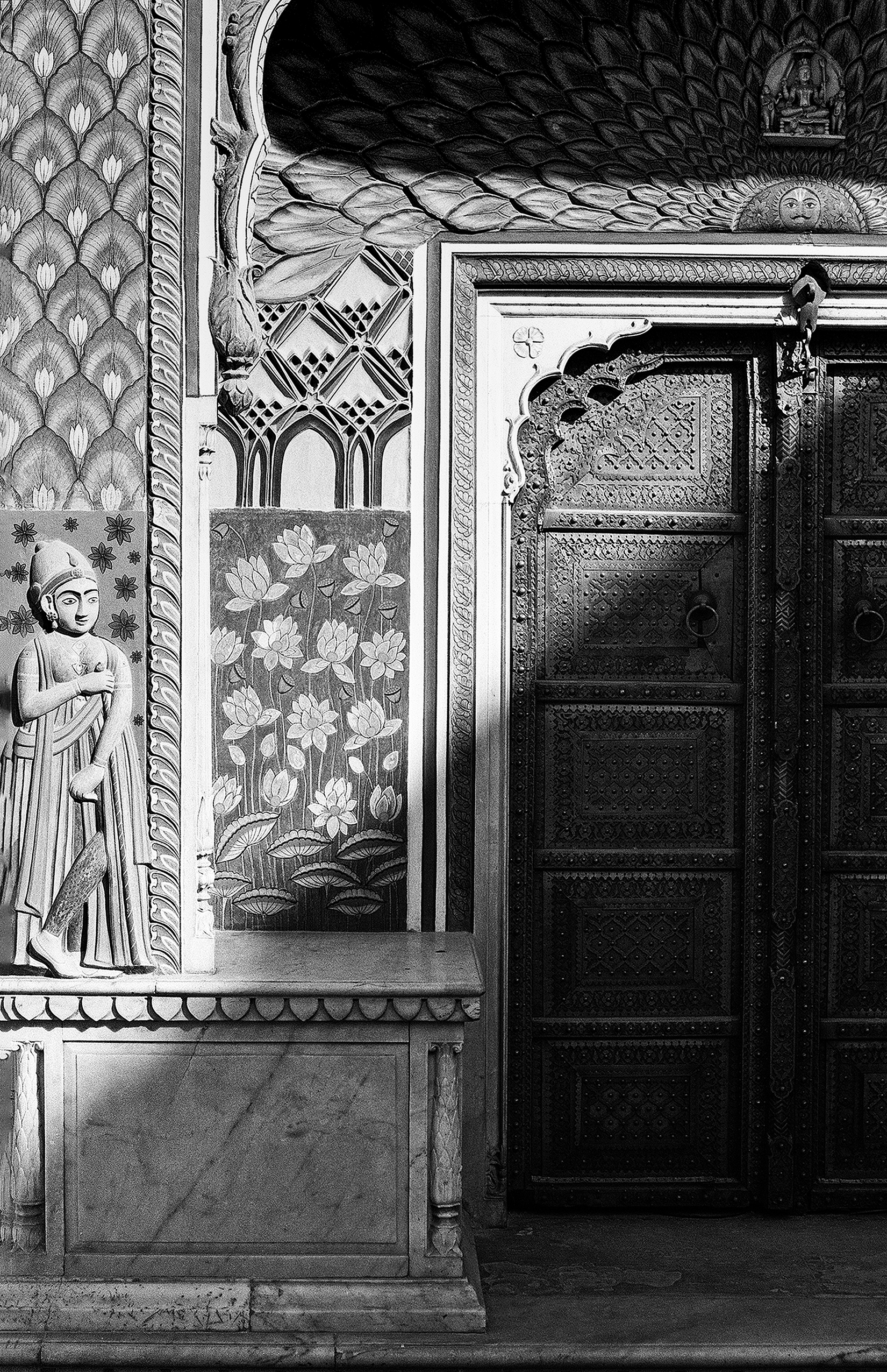 Black and white ornate temple interior with decorated doors featuring detailed lotus flower carvings and religious statues
