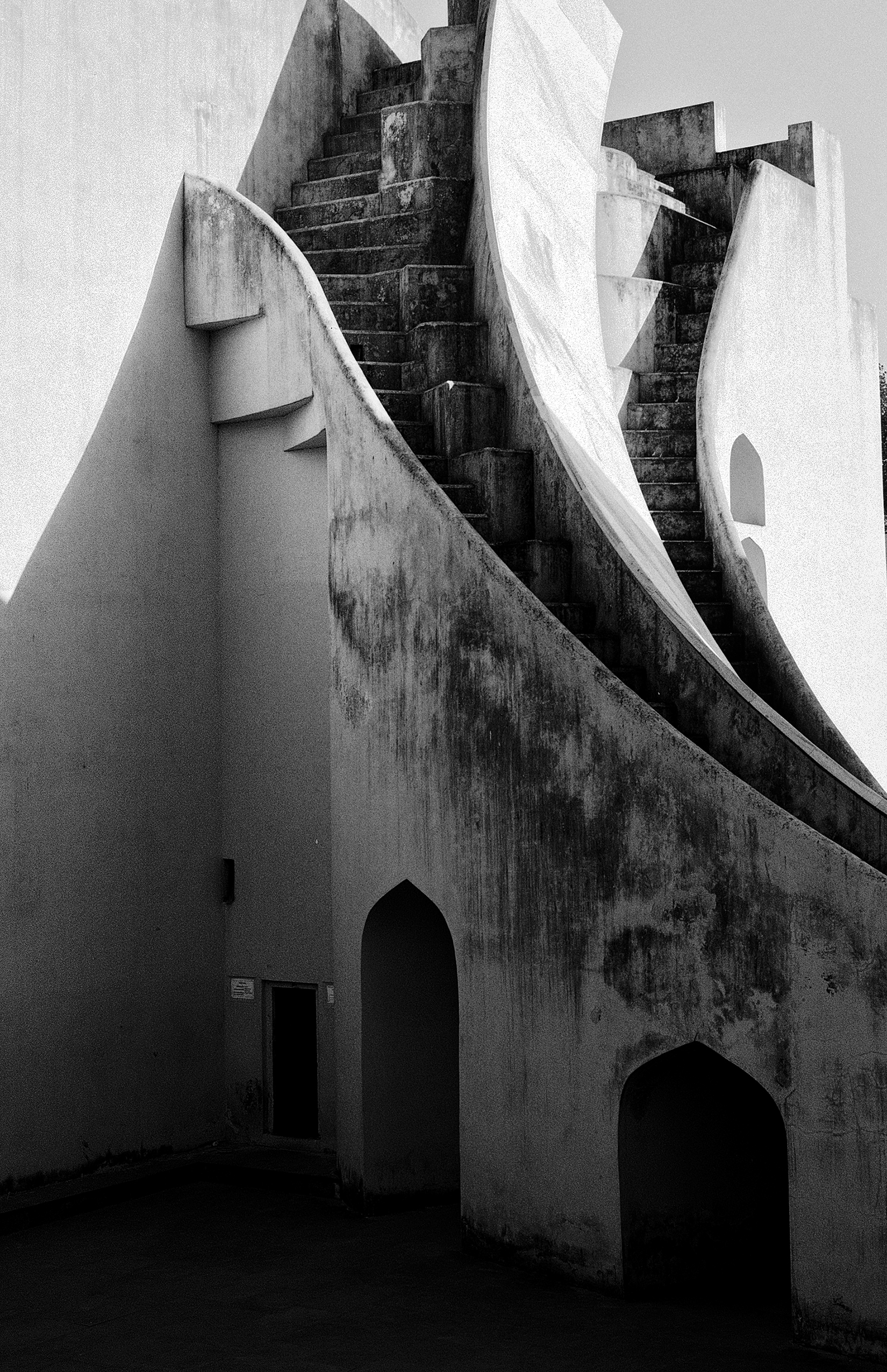 Black and white architectural study curved white staircase dramatic shadows arched doorways