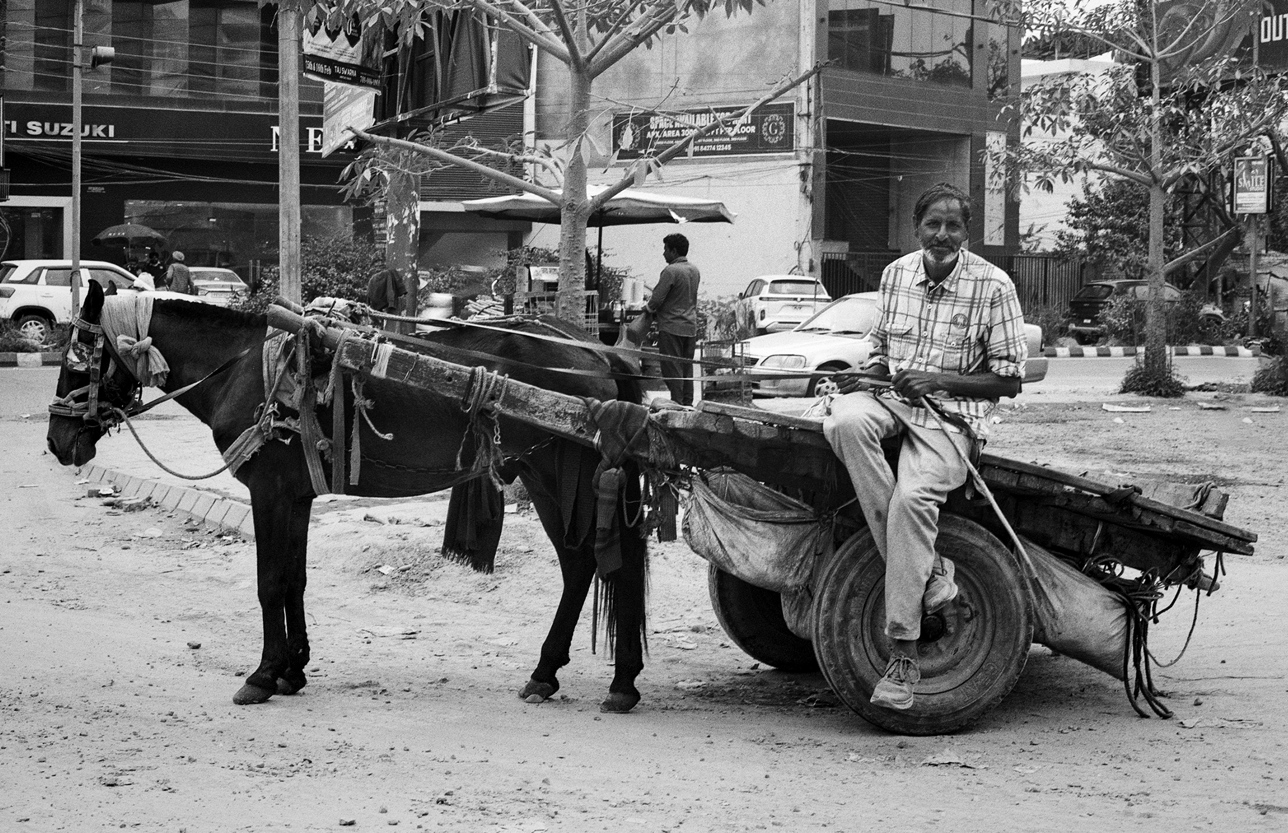 Black and white man smiling with traditional horse-drawn cart loaded with goods on city street