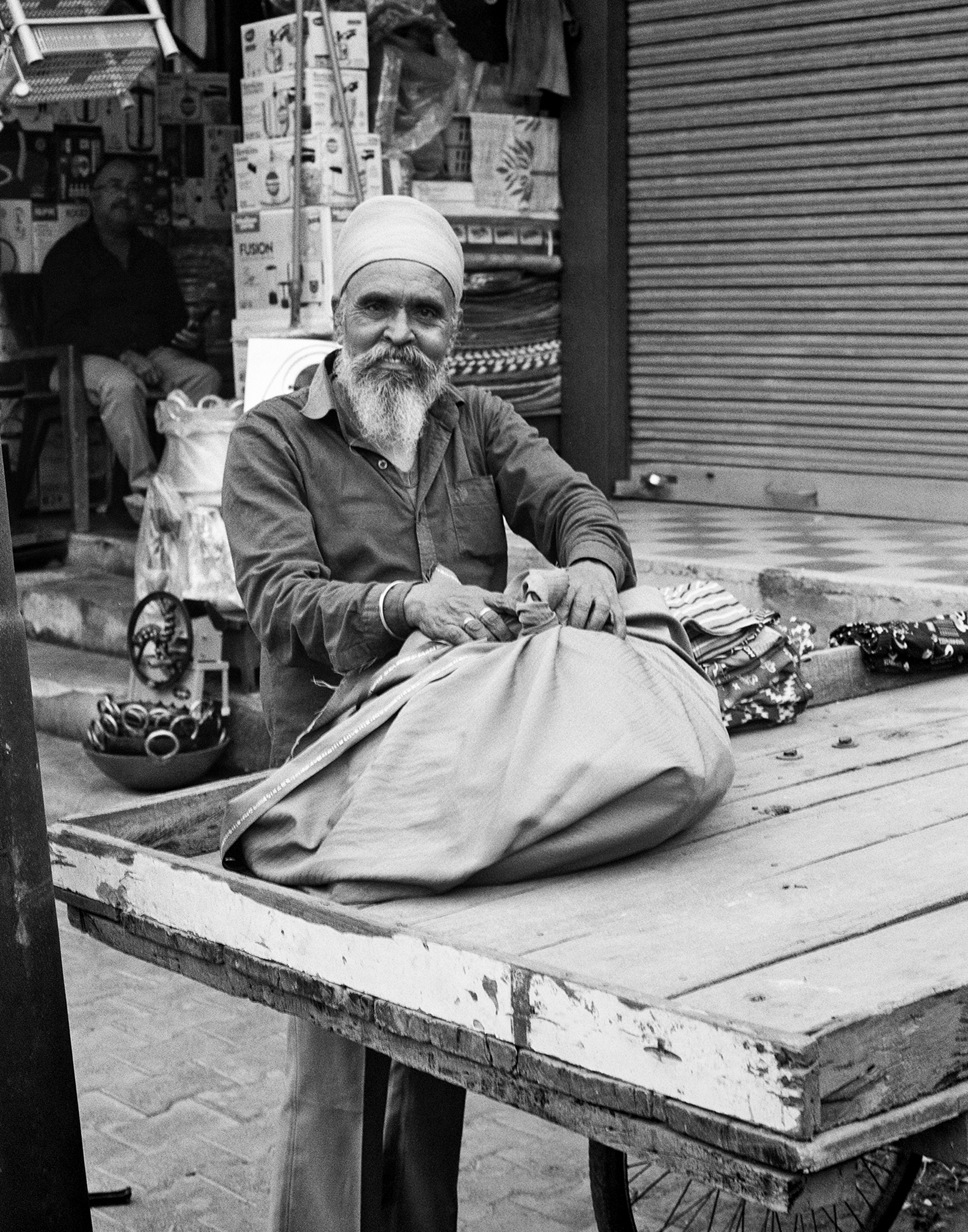 Black and white elderly man with white beard in turban preparing fabric cloth on work table