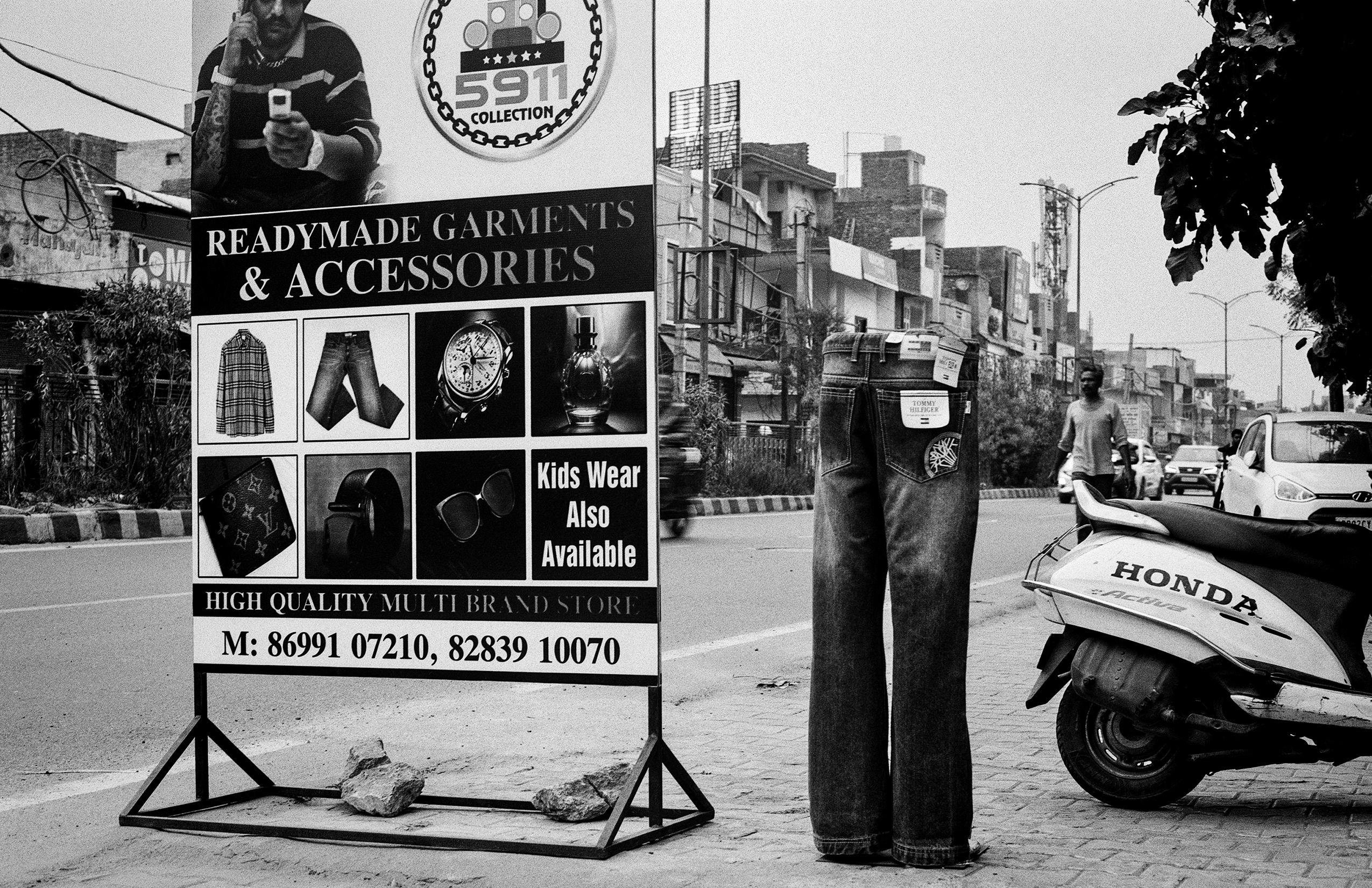 Black and white readymade garments shop storefront with mannequin display and Honda scooter on street