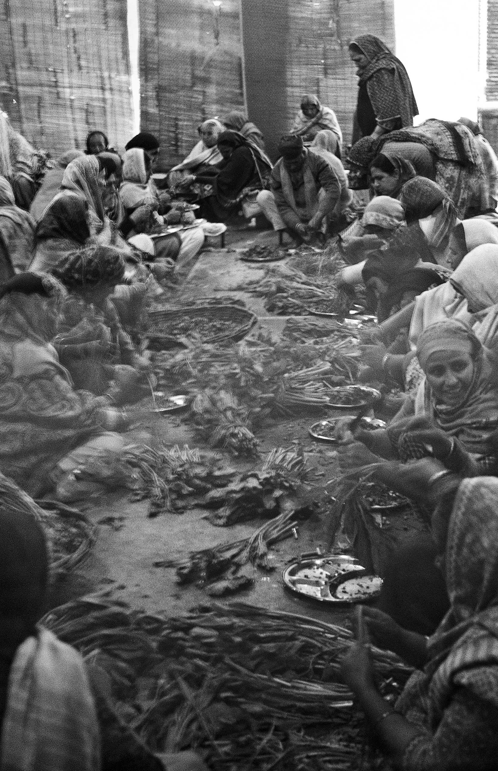 Black and white large crowd gathered on ground in traditional dress eating together outdoor community feast