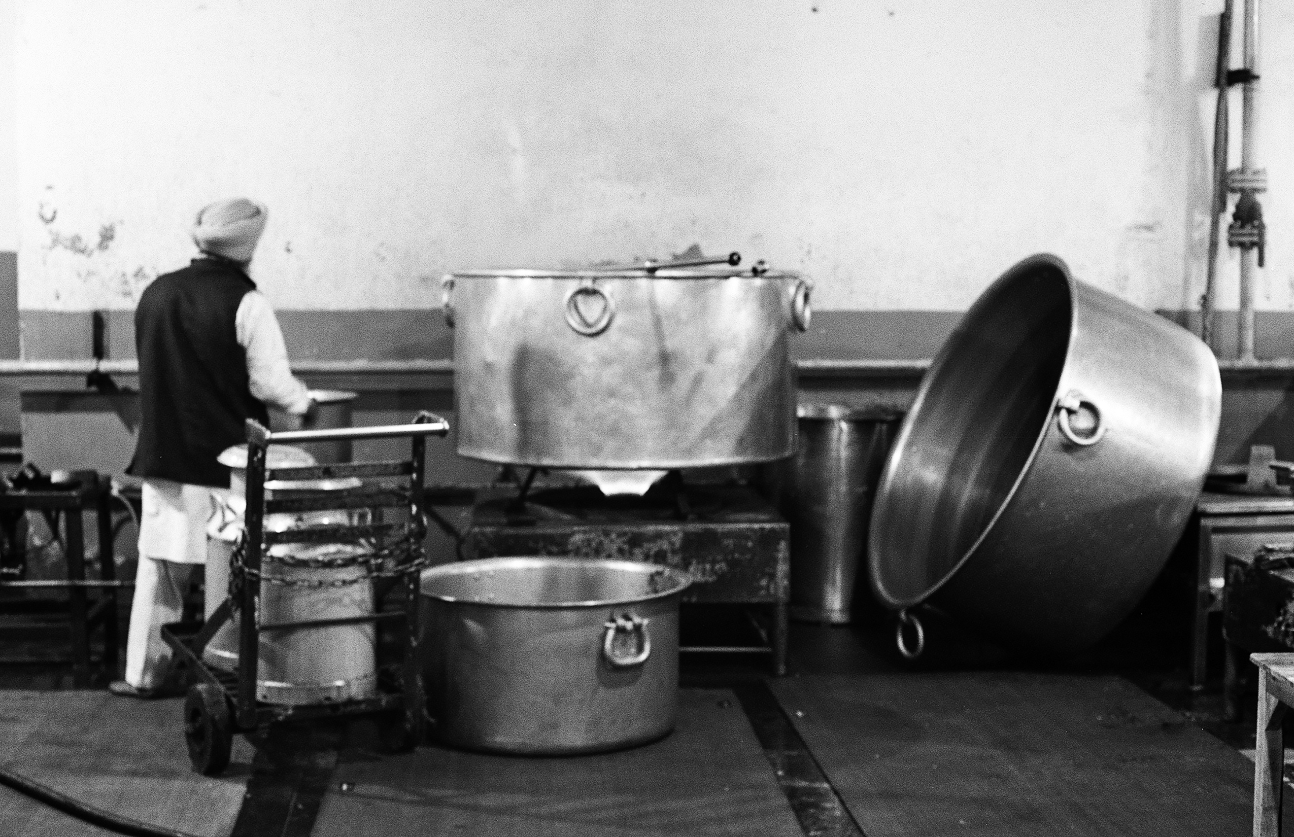 Black and white industrial kitchen worker preparing meal with large metal cooking vessels