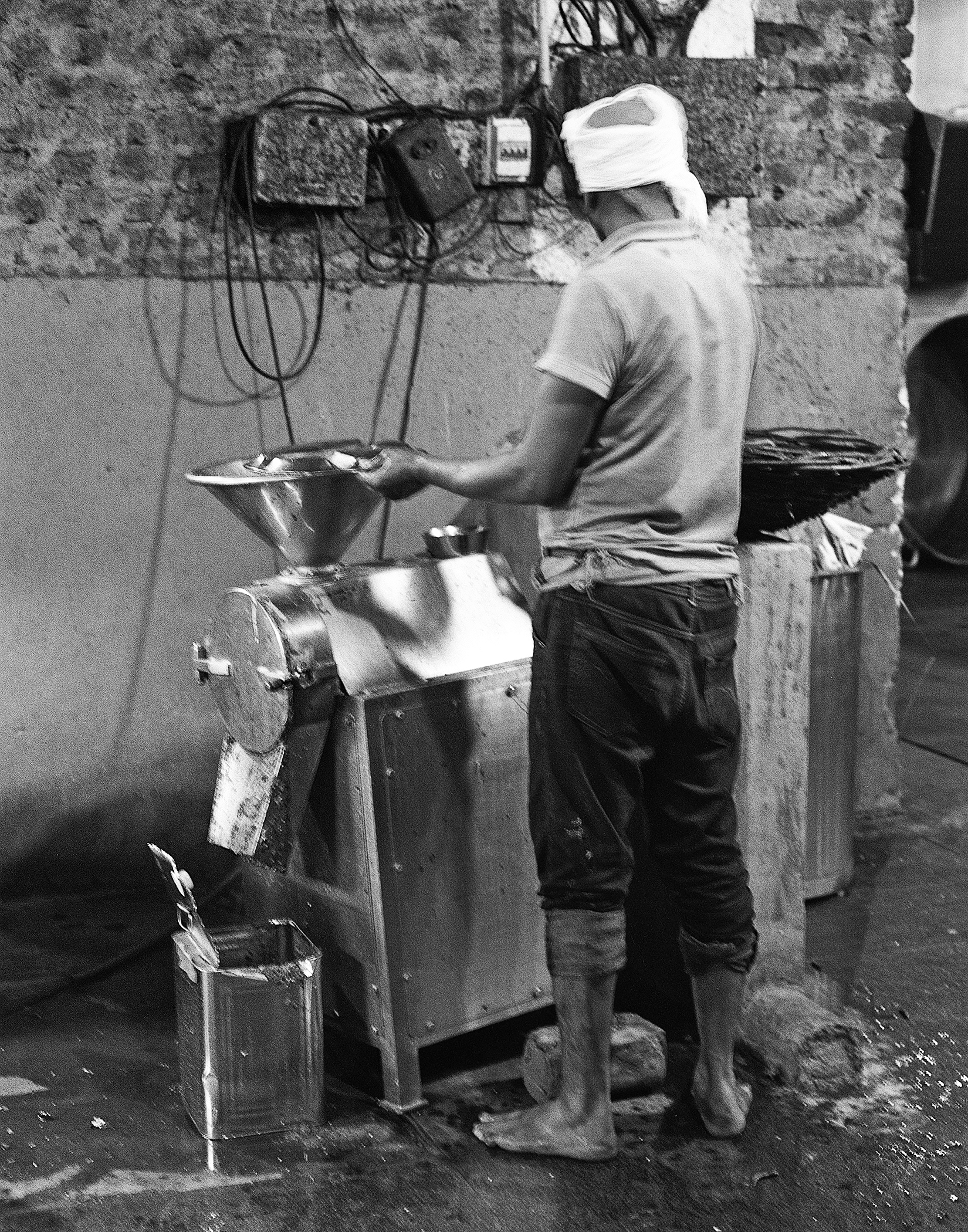 Black and white man operating traditional grain mill with hand crank and decorative cloth above