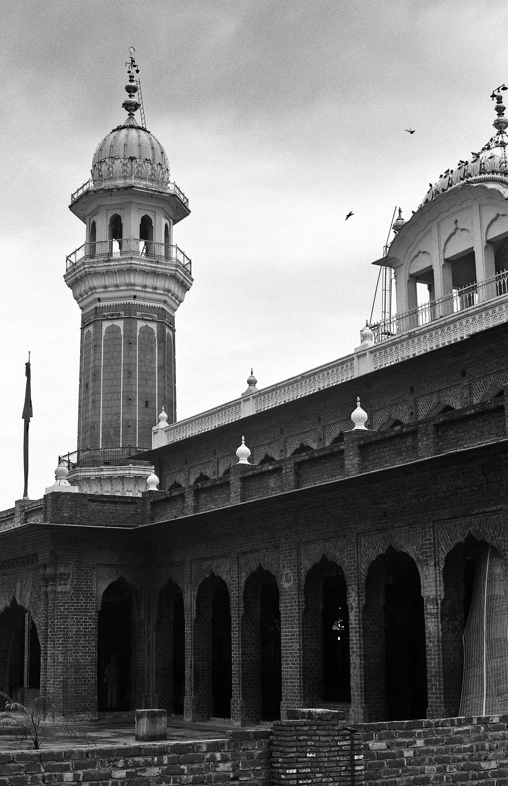 Black and white Jama Masjid mosque with tall minaret arched colonnade and pilgrims on courtyard