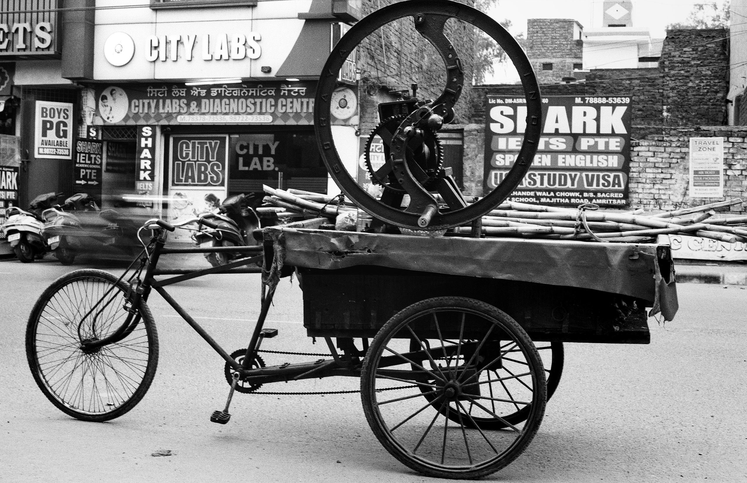Black and white hand-pulled cart with large wooden wheel on street with business storefronts