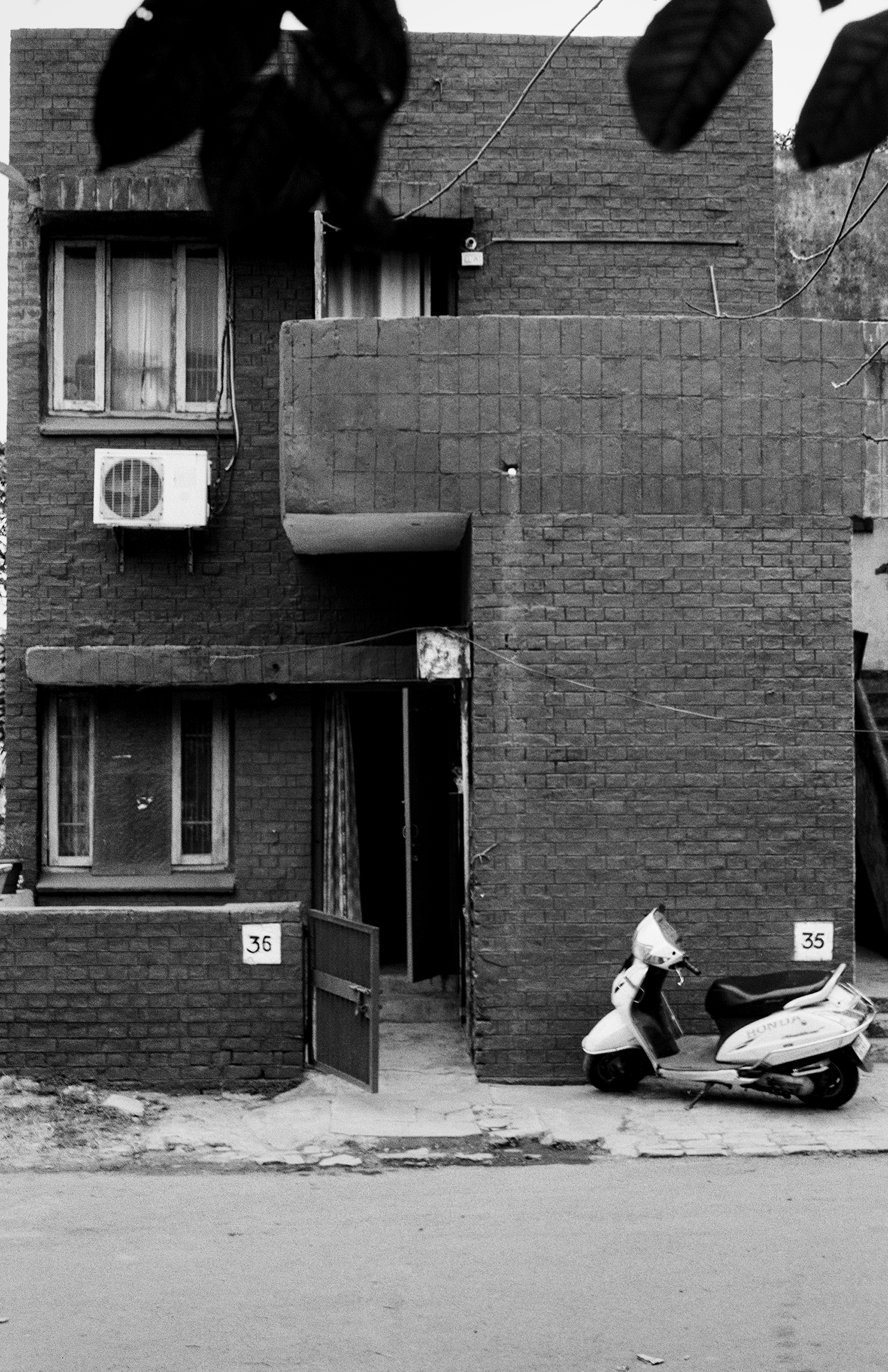 Black and white residential brick building with numbered doors small windows and parked scooter