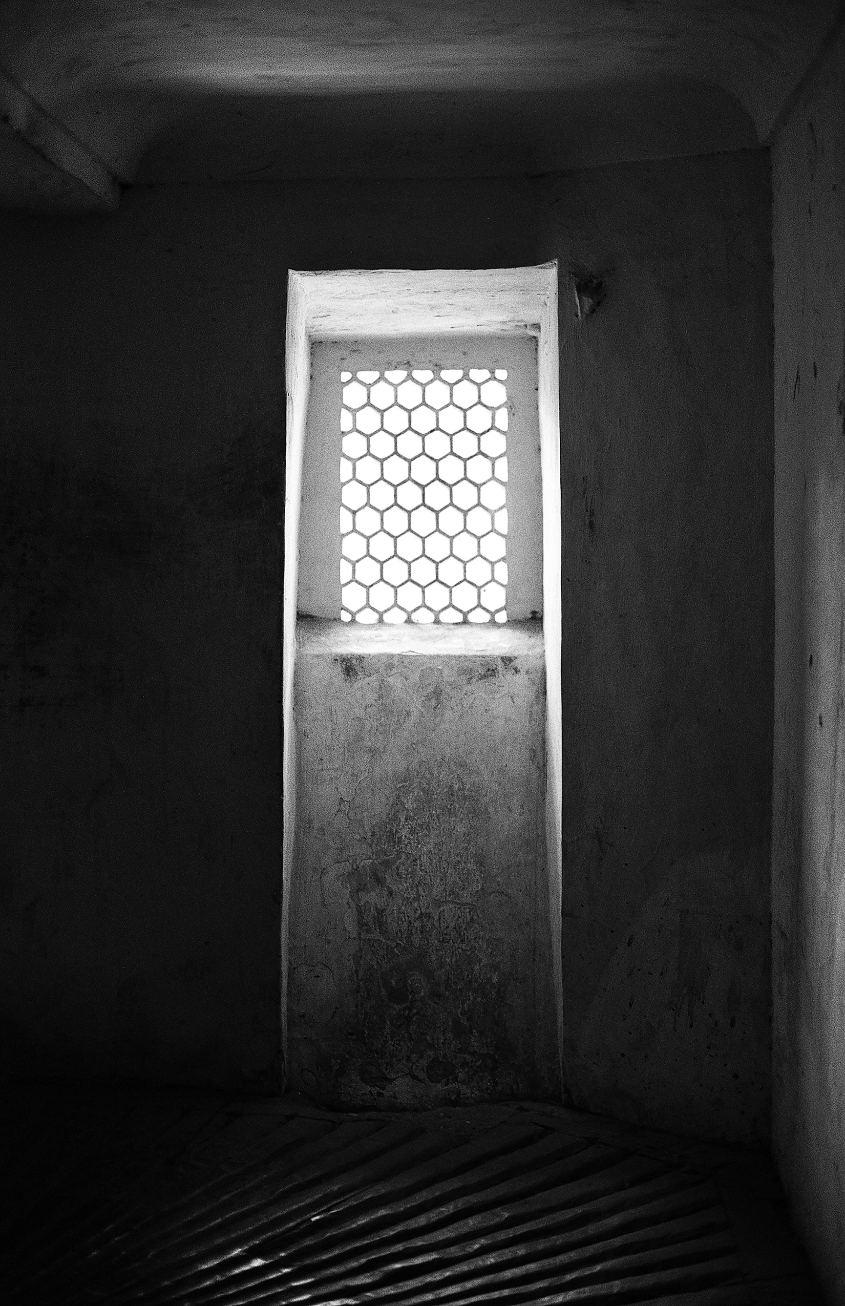 Black and white interior corridor with hexagonal ventilation window framing bright geometric pattern