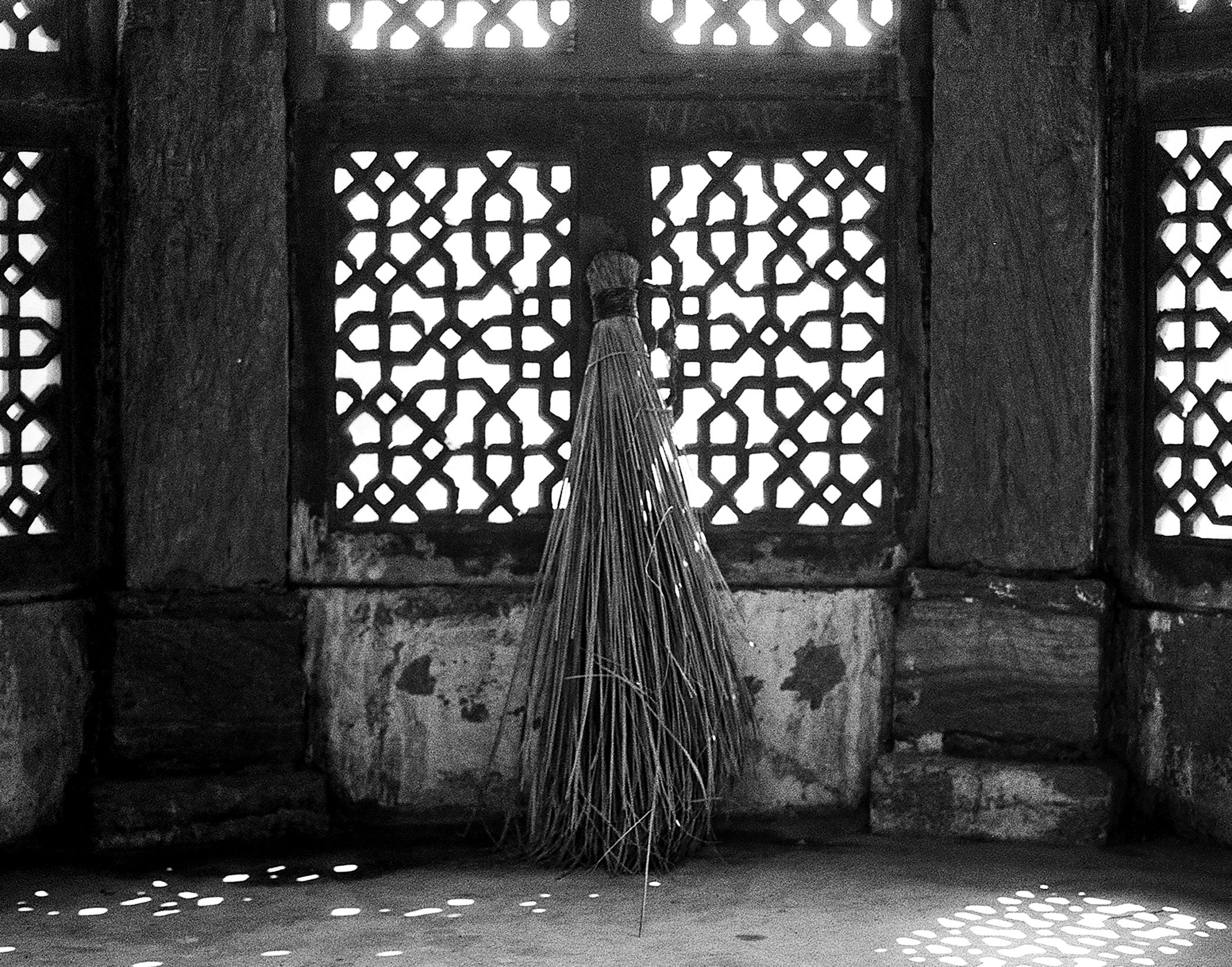 Black and white figure in white burqa standing before ornate lattice screens and geometric patterns