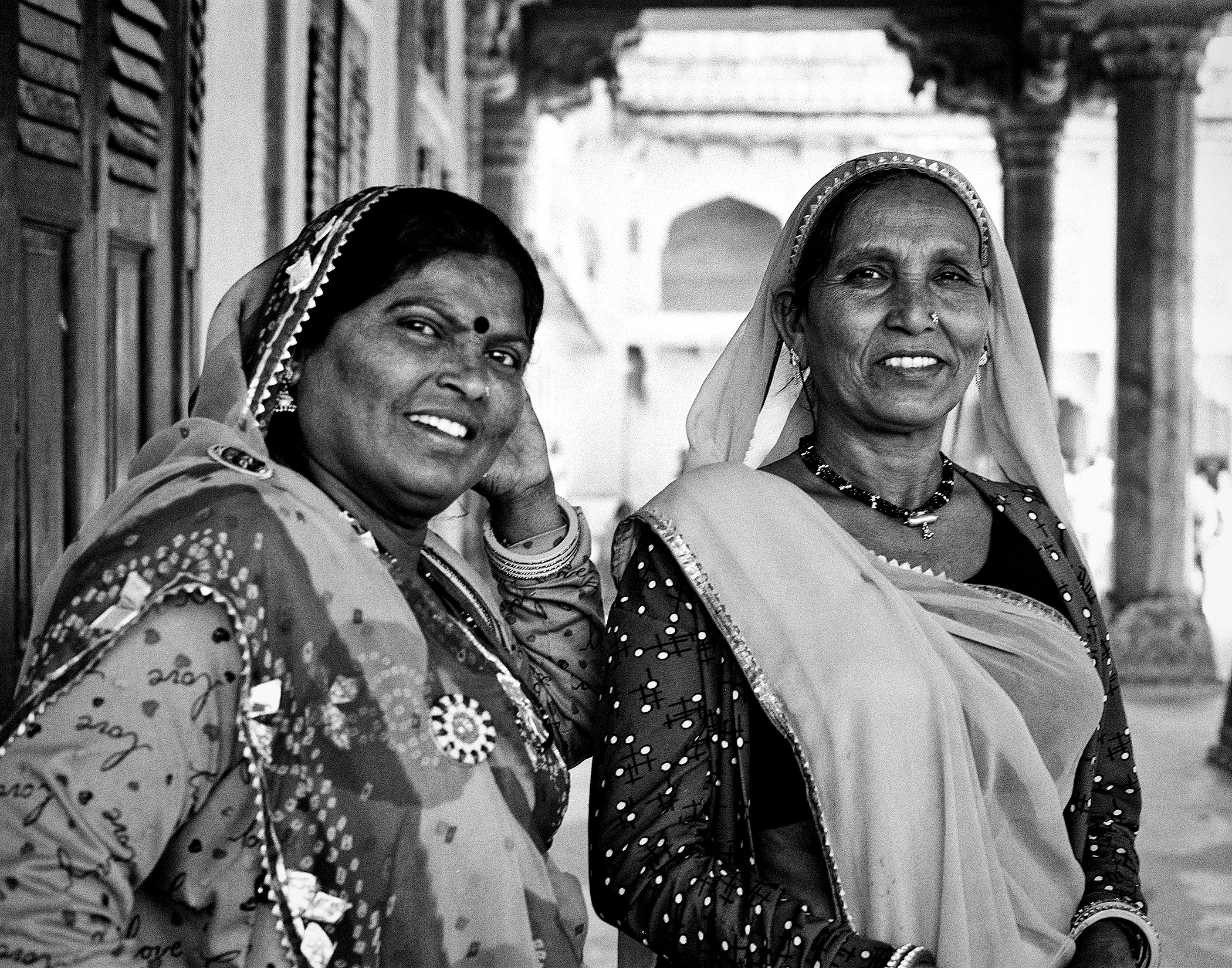 Black and white two women in traditional dress with decorative garments headdresses and jewelry smiling